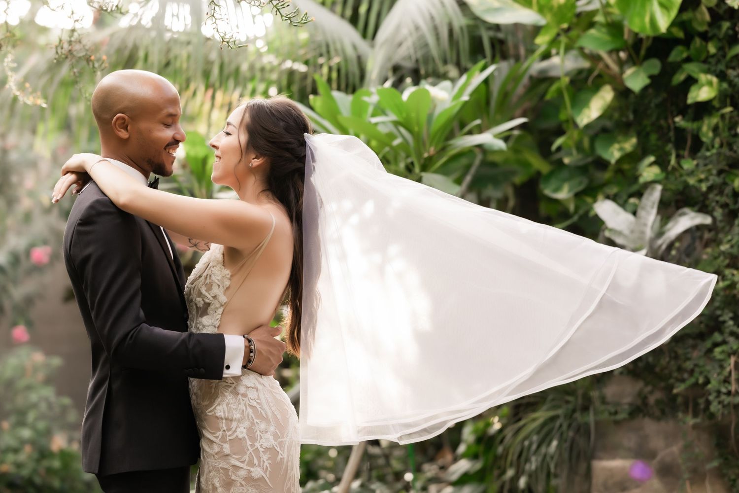 Dynamic wedding portrait with bride's veil flowing in the breeze against tropical garden backdrop.