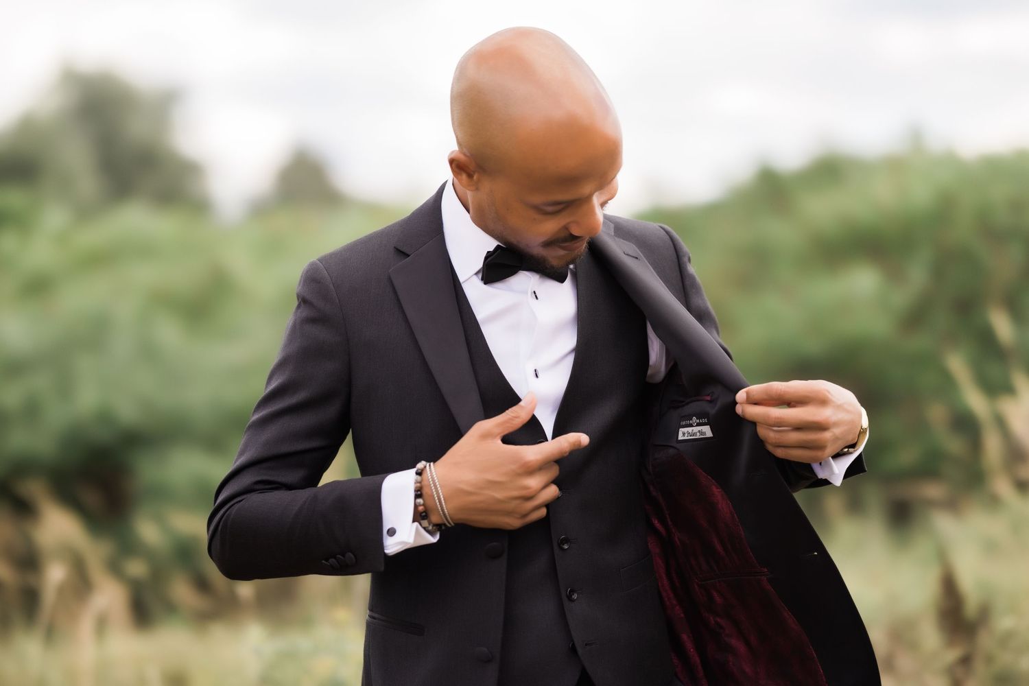 Groom adjusts formal tuxedo jacket in candid outdoor photo.