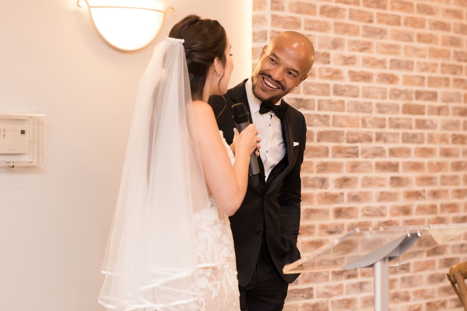 A candid moment of laughter between newlyweds against a brick wall backdrop.