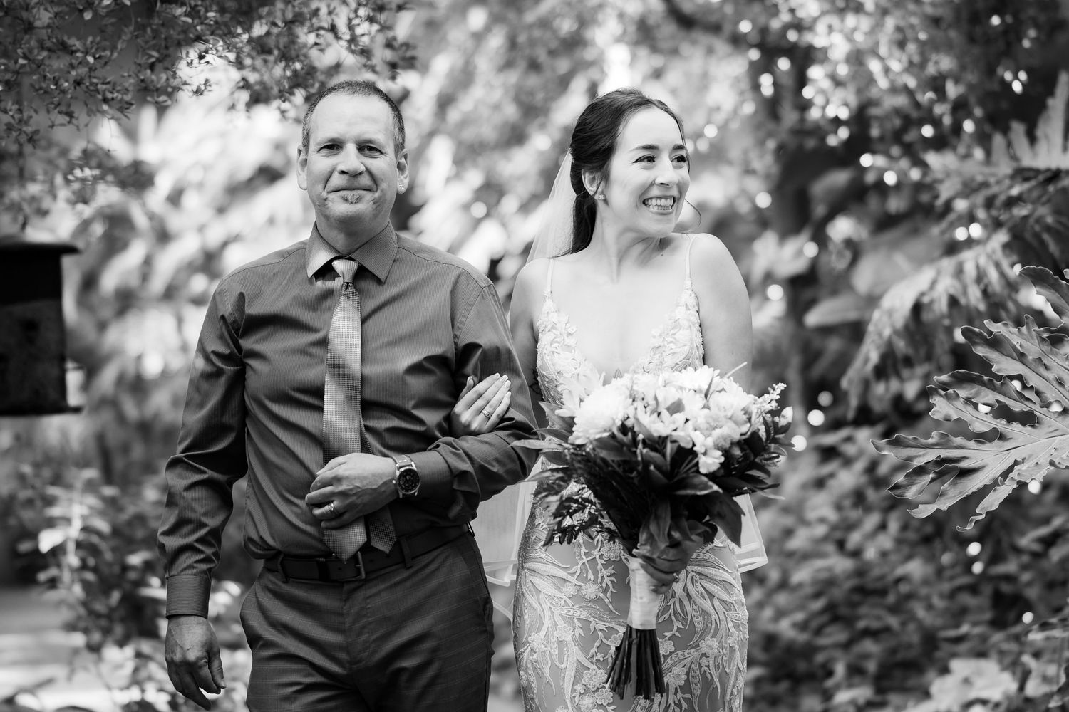Black and white portrait of a couple walking through a garden pathway.