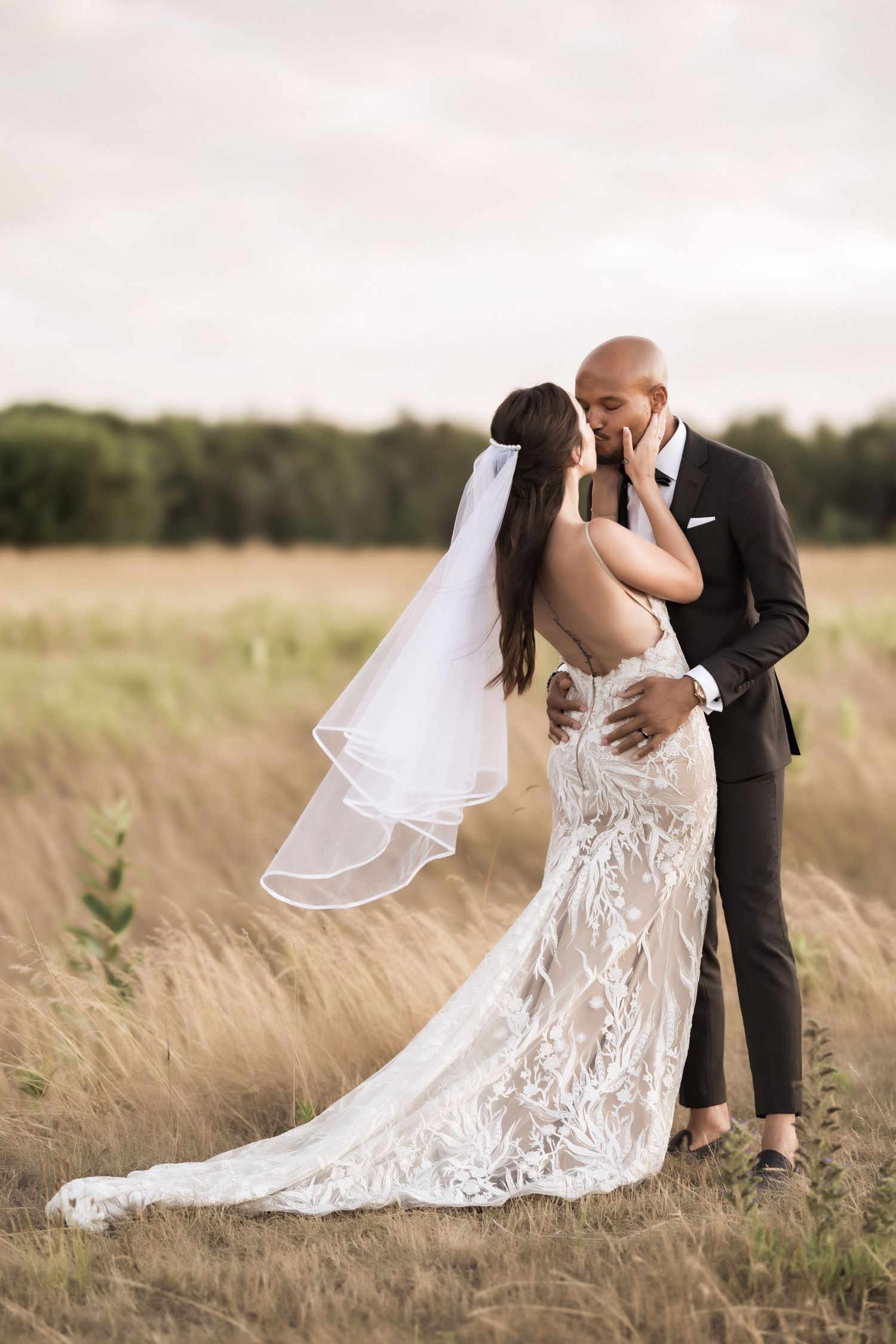 A romantic wedding photo of newlyweds sharing an intimate moment in a golden wheat field at sunset.