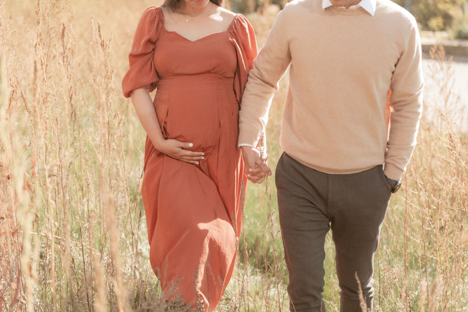 Side view of expecting couple walking together through golden grass field.