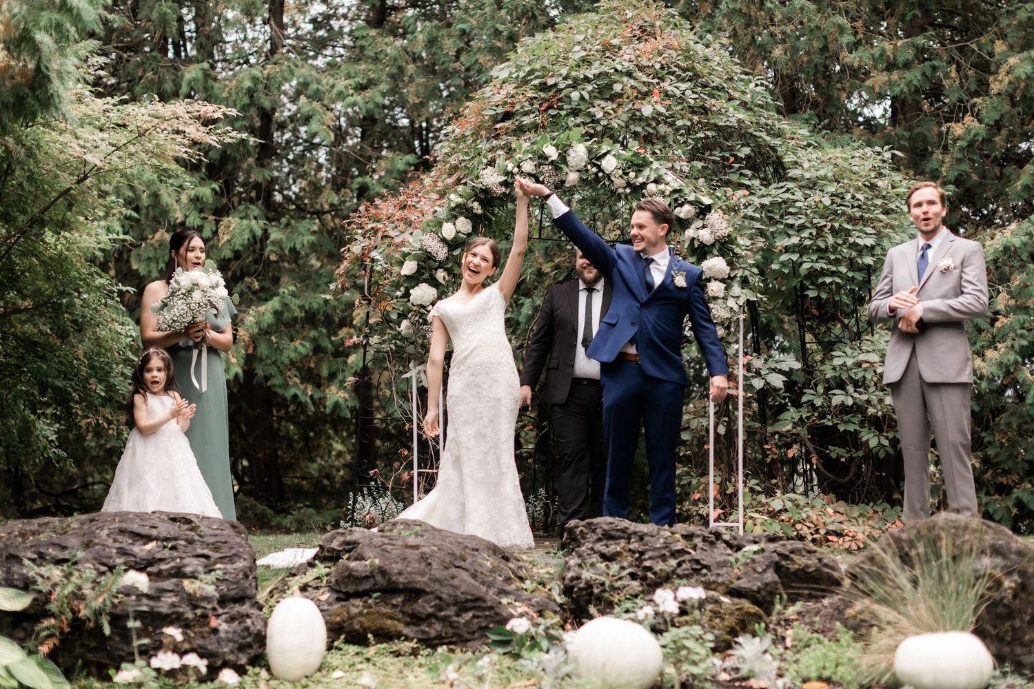 Joyful celebration moment during an outdoor garden wedding ceremony with white pumpkin decorations.