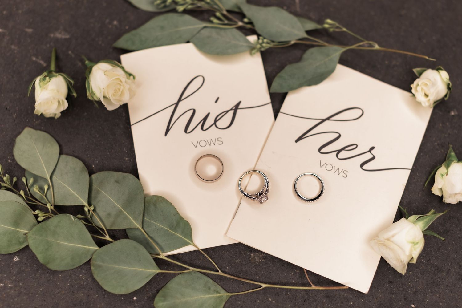 Wedding rings displayed on his and her cards with white roses and eucalyptus.