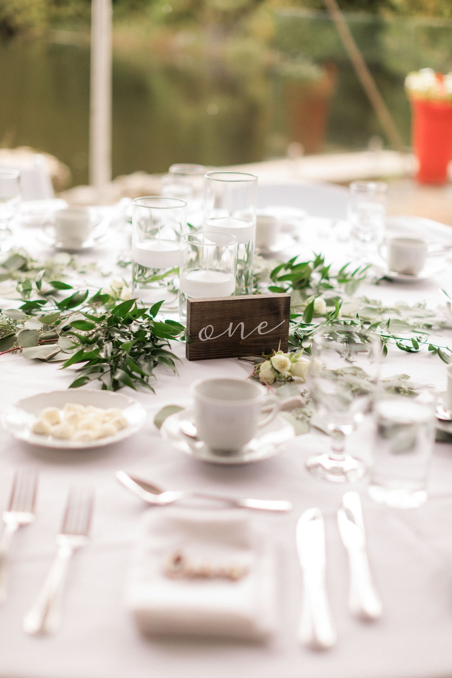 Elegant table setting with greenery garland and minimalist table number at wedding reception.
