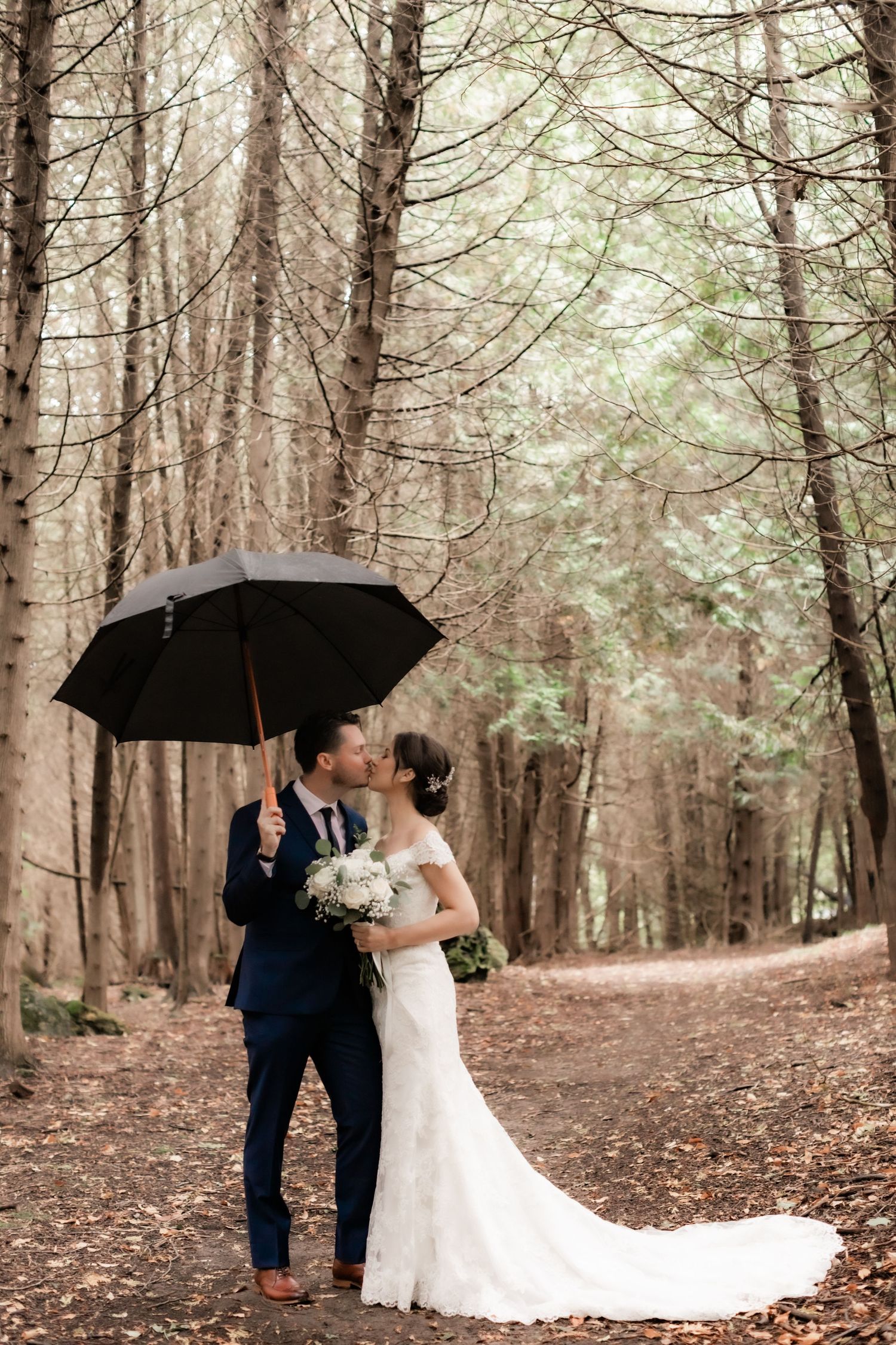 Wedding couple embracing under black umbrella in misty forest setting with beautiful natural lighting.