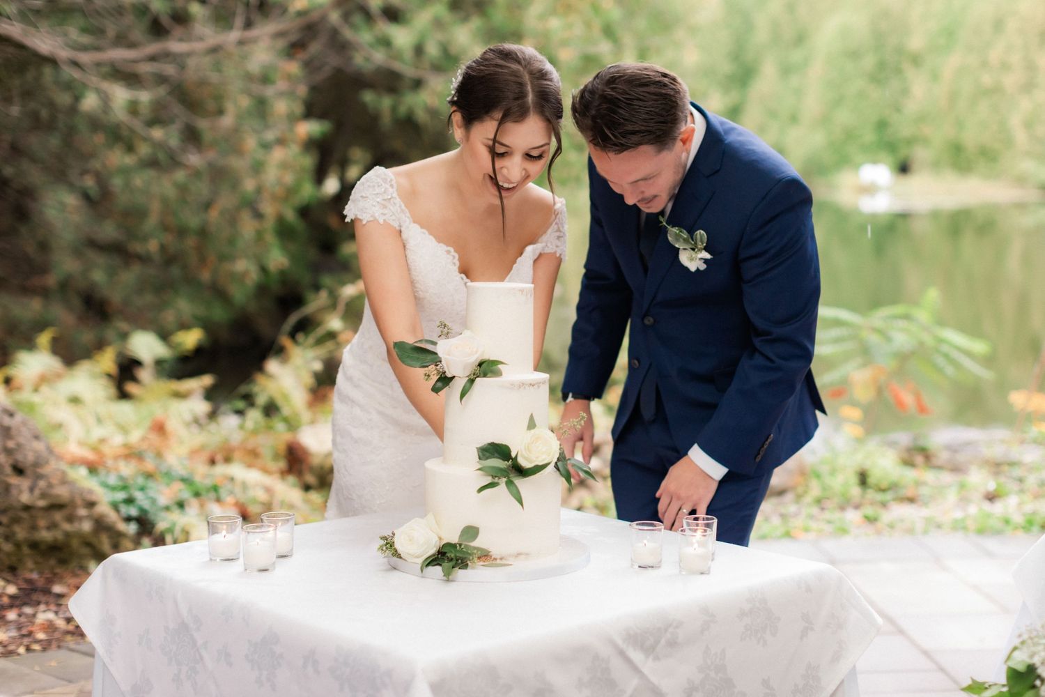 A couple cuts their elegant white wedding cake together at their outdoor reception.