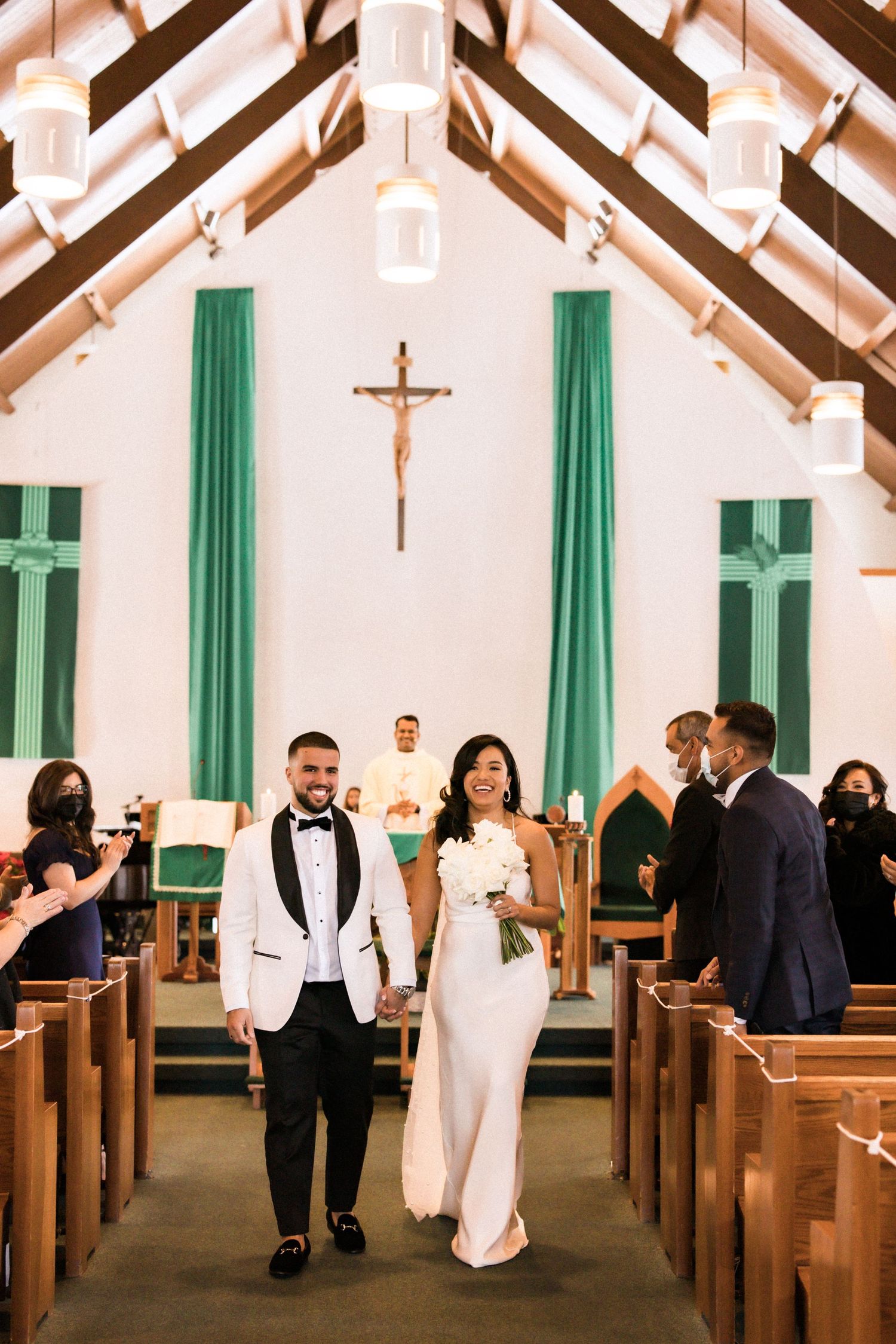 Happy couple walks down aisle after church ceremony as guests celebrate.