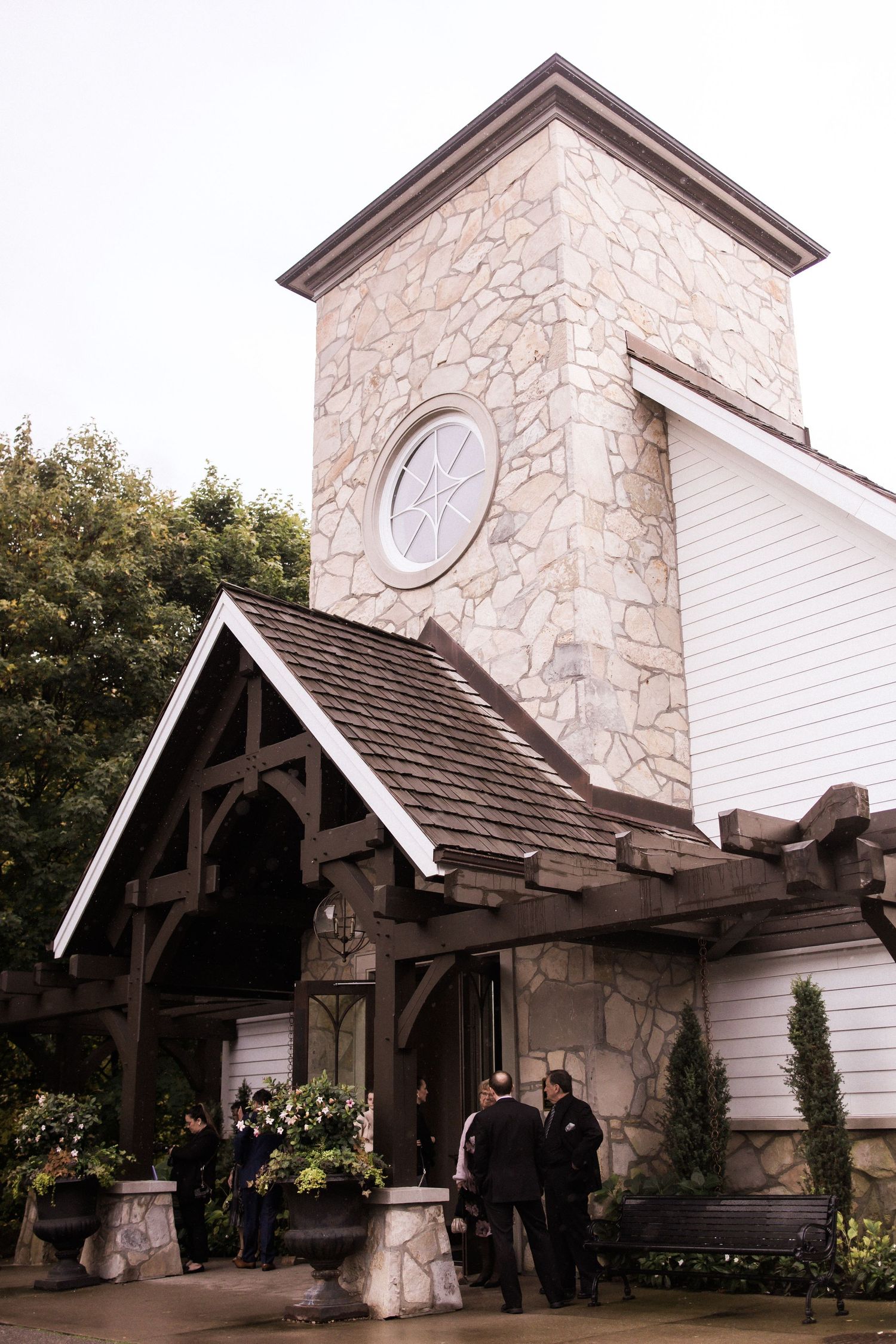 Stone chapel exterior with timber frame entrance and decorative flower arrangements.