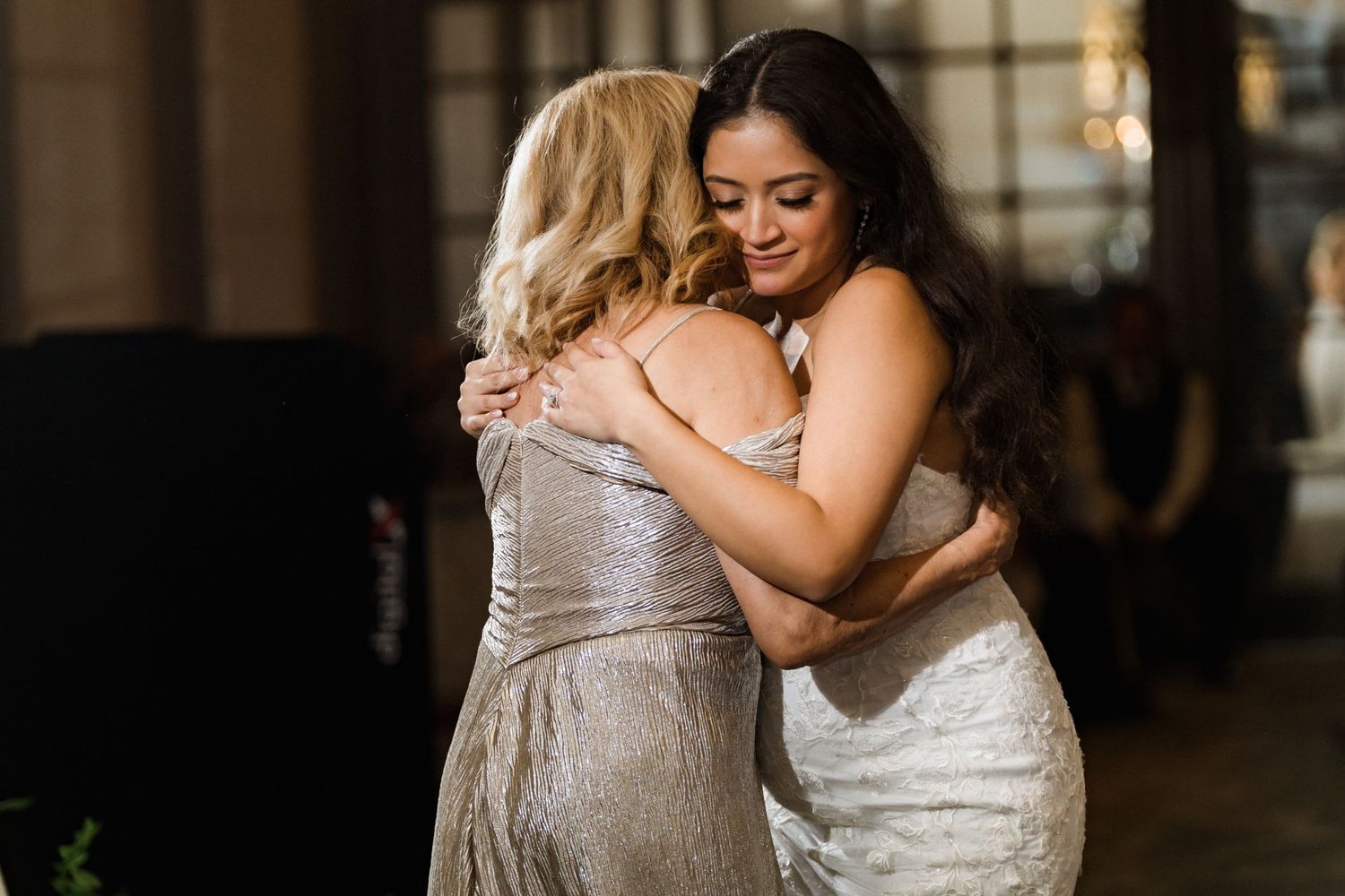 Two people share an emotional embrace at an indoor wedding reception.