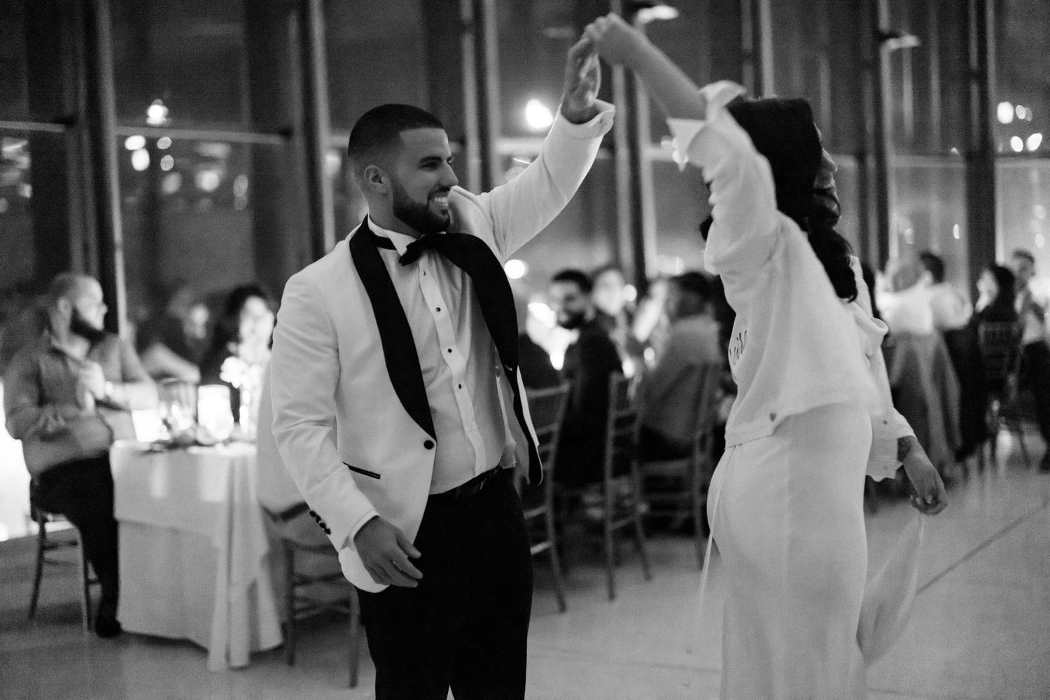 A joyful dance moment in black and white as a couple twirls in formal attire.
