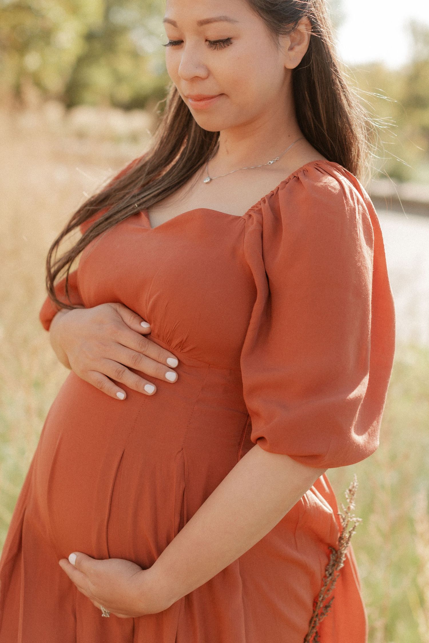 Close-up maternity portrait featuring rust-colored dress with sweetheart neckline.