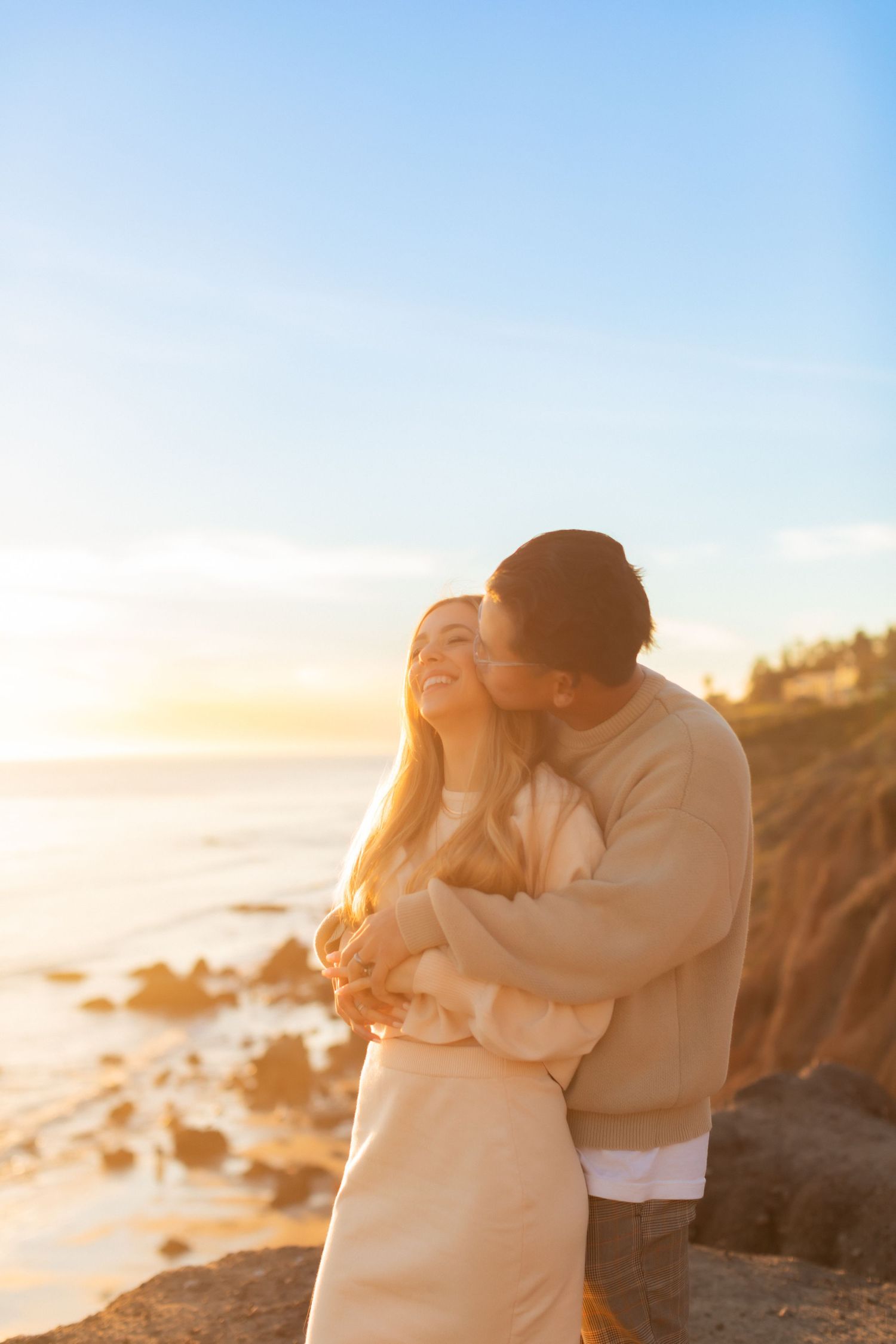 Tender moment between couple against dramatic coastal sunset backdrop.