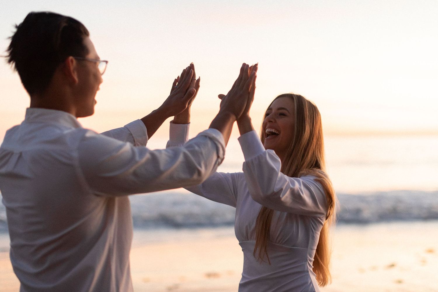 Joyful couple giving high fives while standing on beach at sunset.