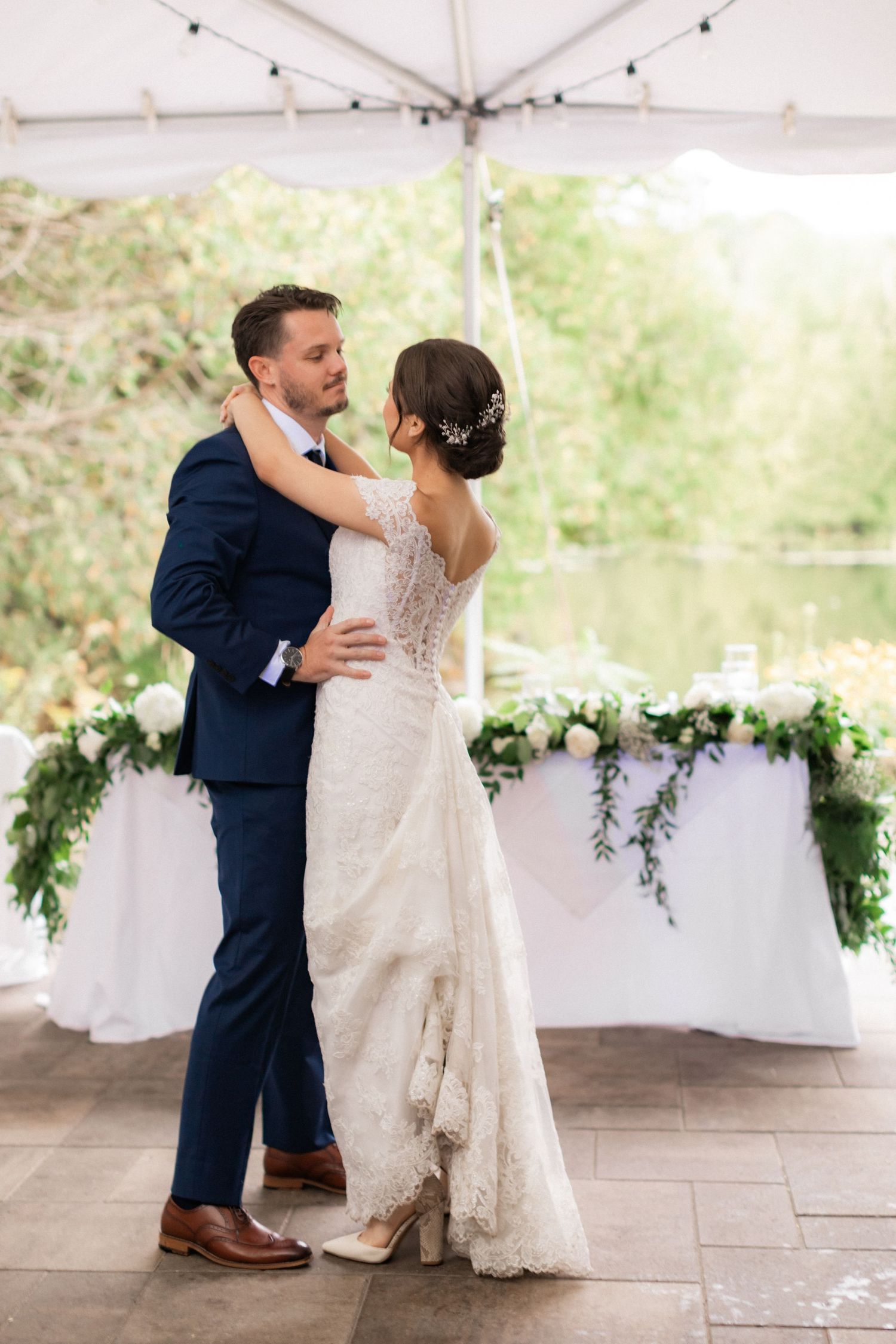 Couple shares their first dance under a white tent decorated with greenery and florals.