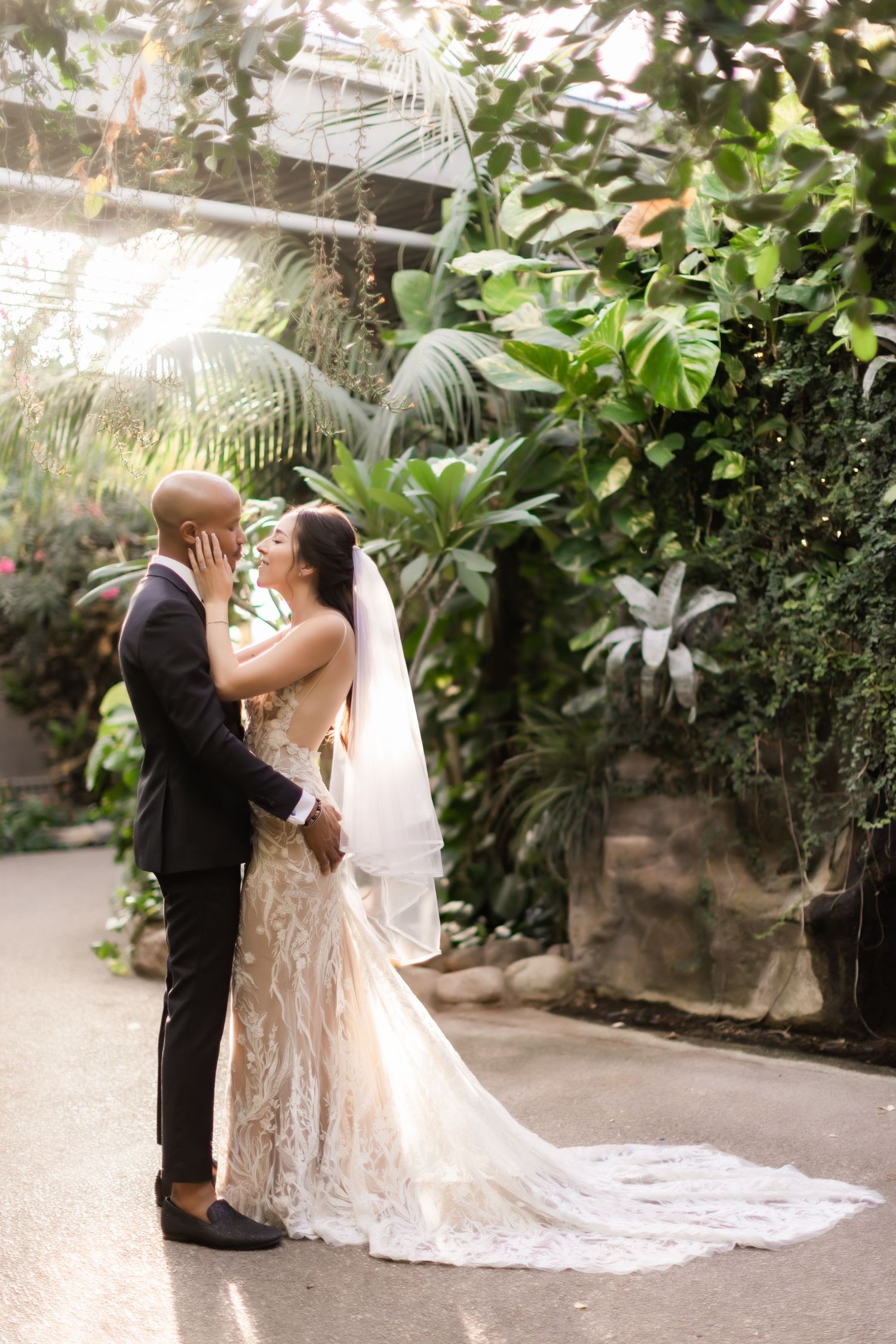 Newlyweds share an intimate moment in a botanical garden path with trailing wedding dress.