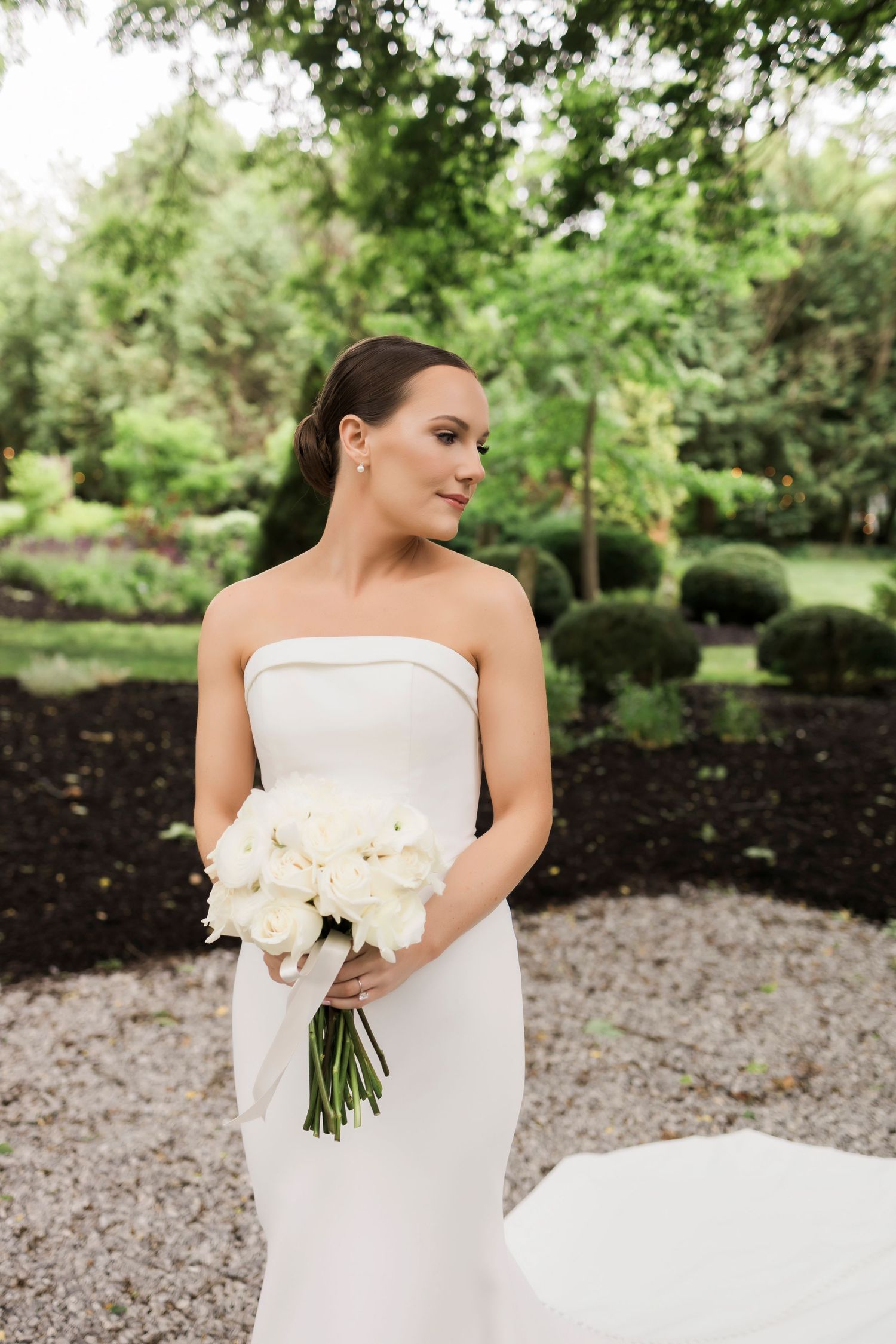 A minimalist white wedding dress photographed in a lush garden setting with manicured landscaping.