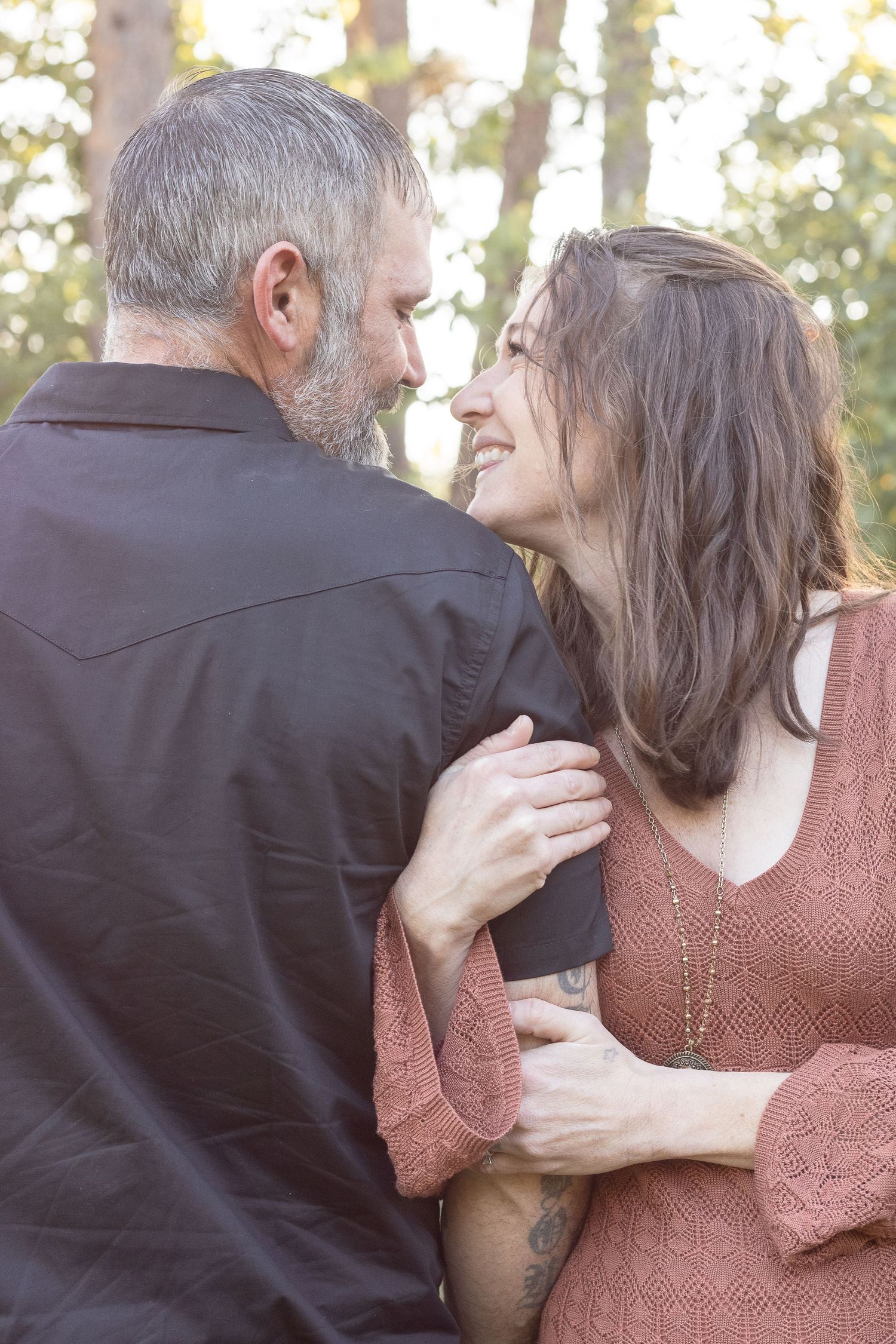 A romantic couple shares an intimate moment outdoors in soft sunlight, wearing dark and rust colored clothing.
