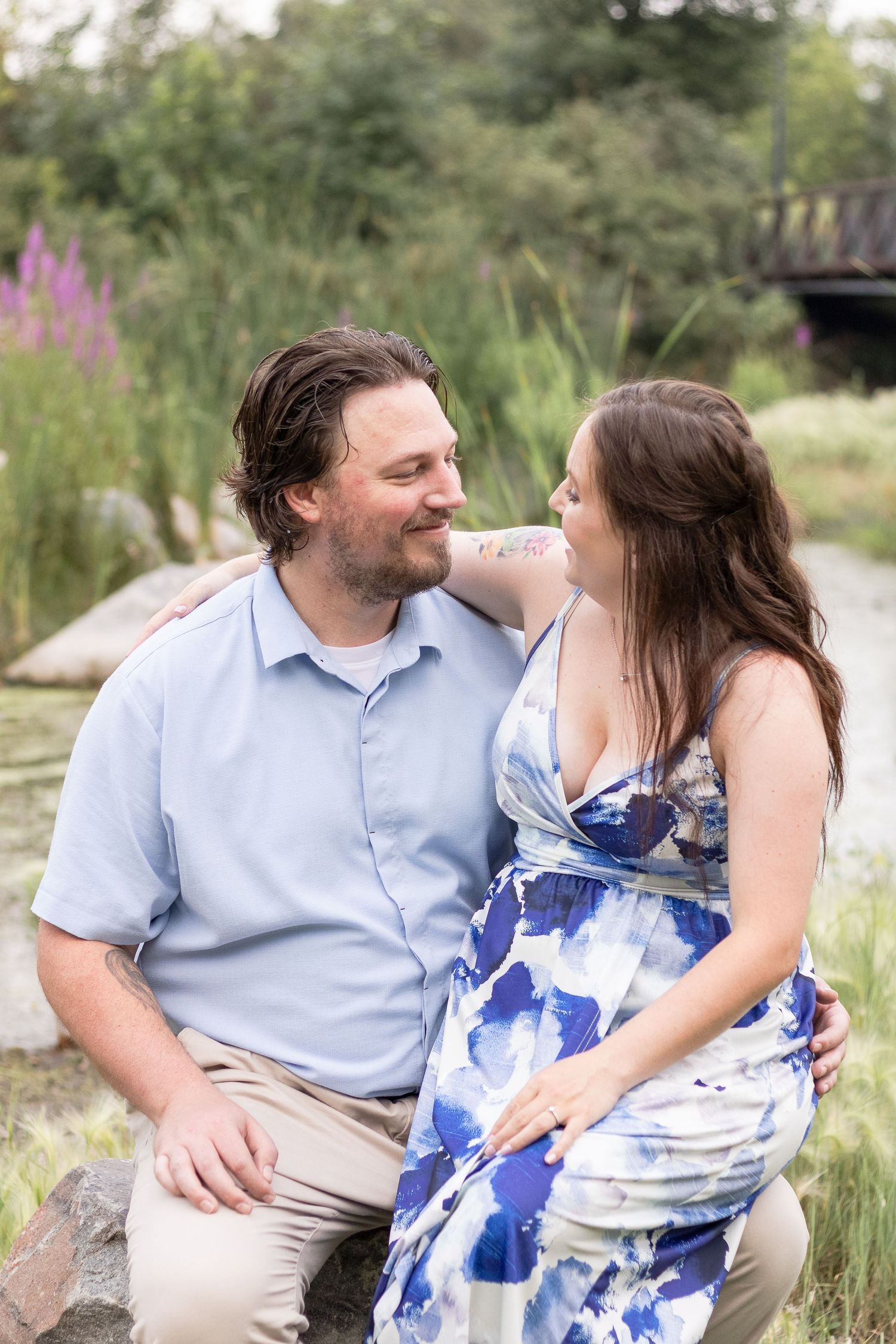 A couple shares a romantic moment by a pond, with a bridge visible in the background.