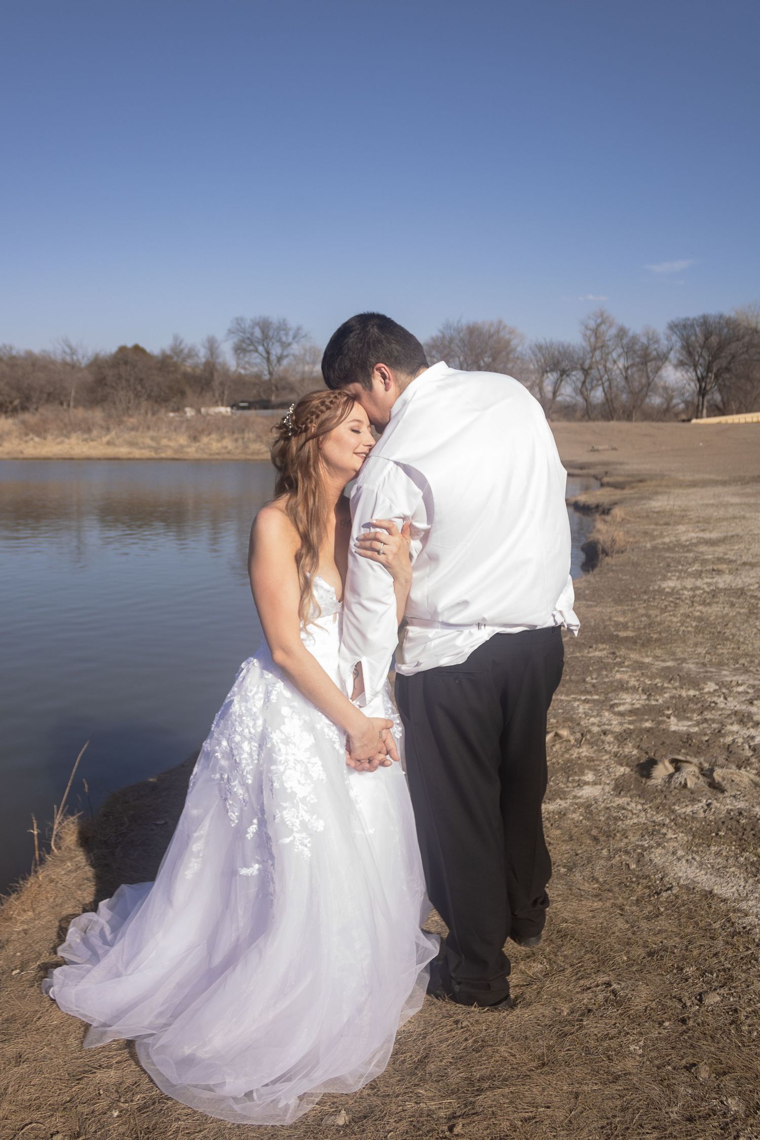 Wedding couple sharing intimate moment by lakeside on sunny winter day.