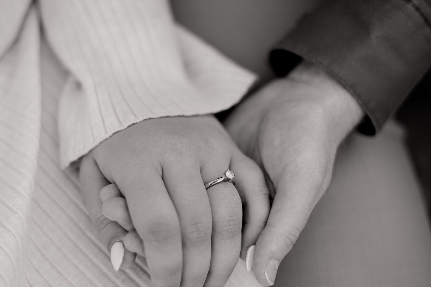 A close-up black and white photo of hands with an engagement ring.