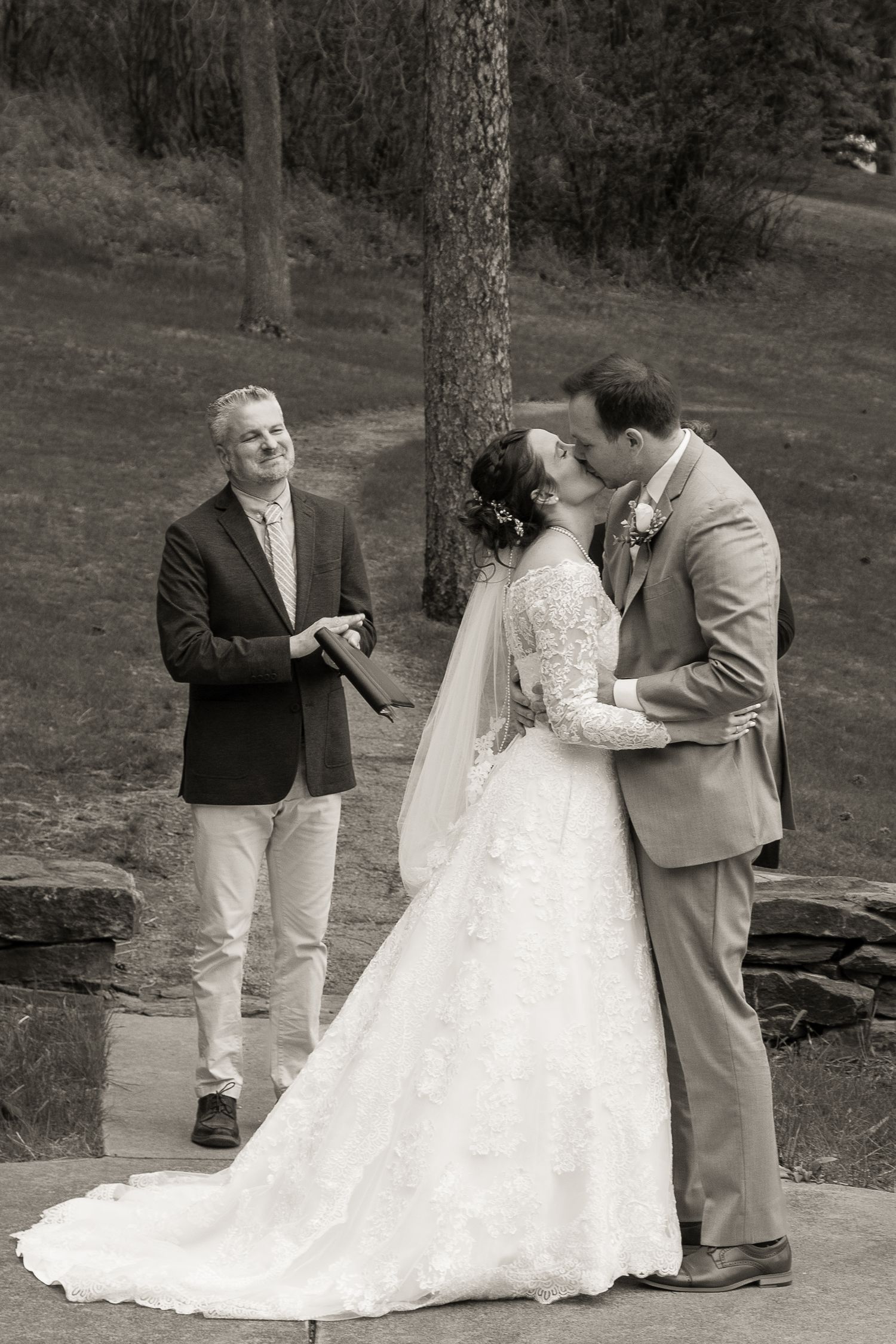 A black and white outdoor ceremony photo captures an intimate wedding moment.