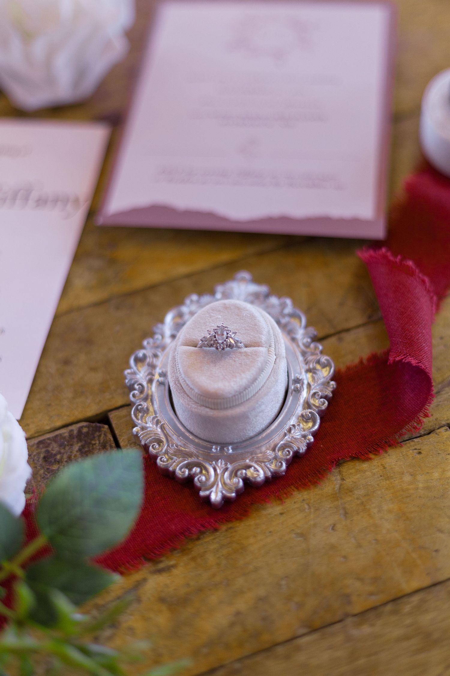 Delicate engagement ring displayed on an ornate silver holder with pink stationery and rose petals.