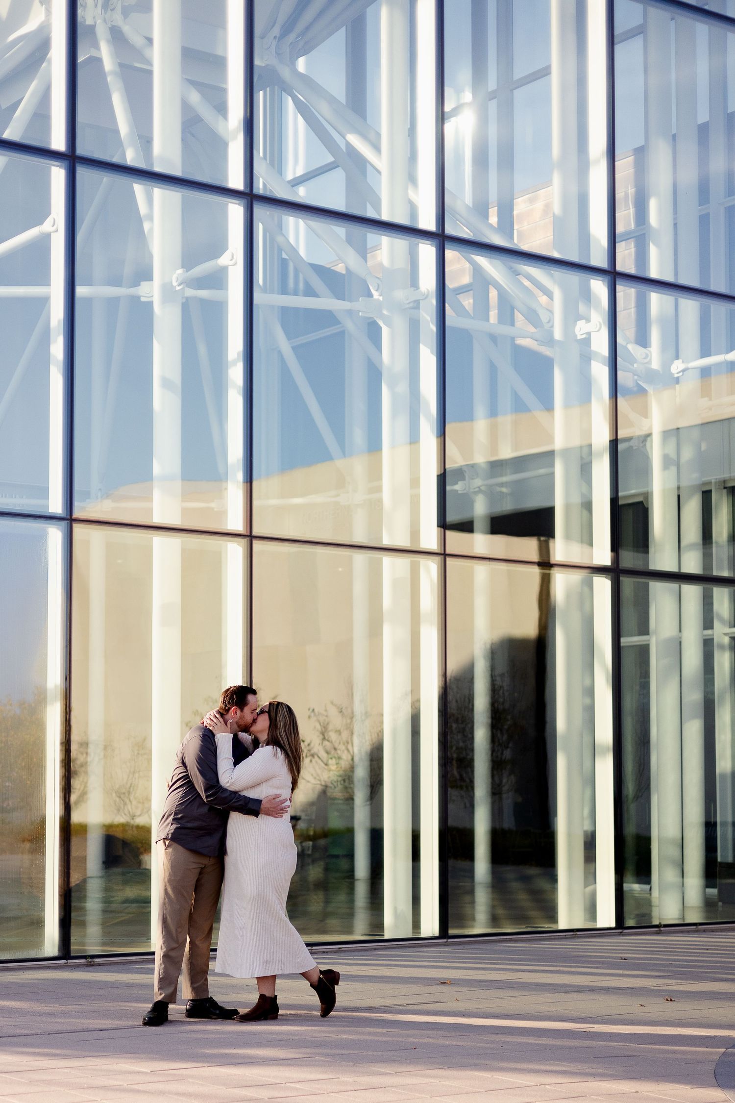 A romantic couple shares a tender moment against a modern glass building exterior.