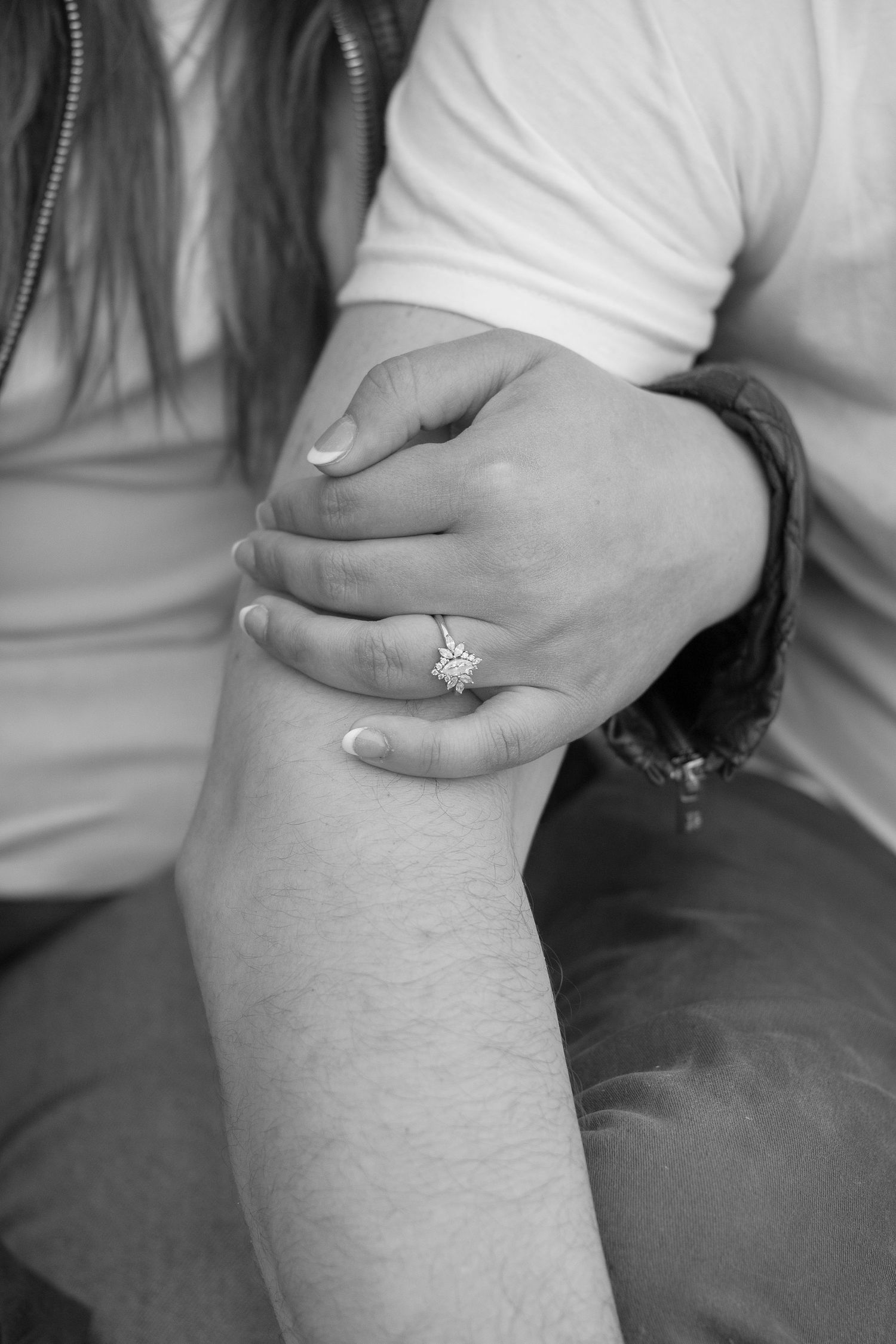 Close-up black and white photo of hands with engagement ring showing tender embrace.