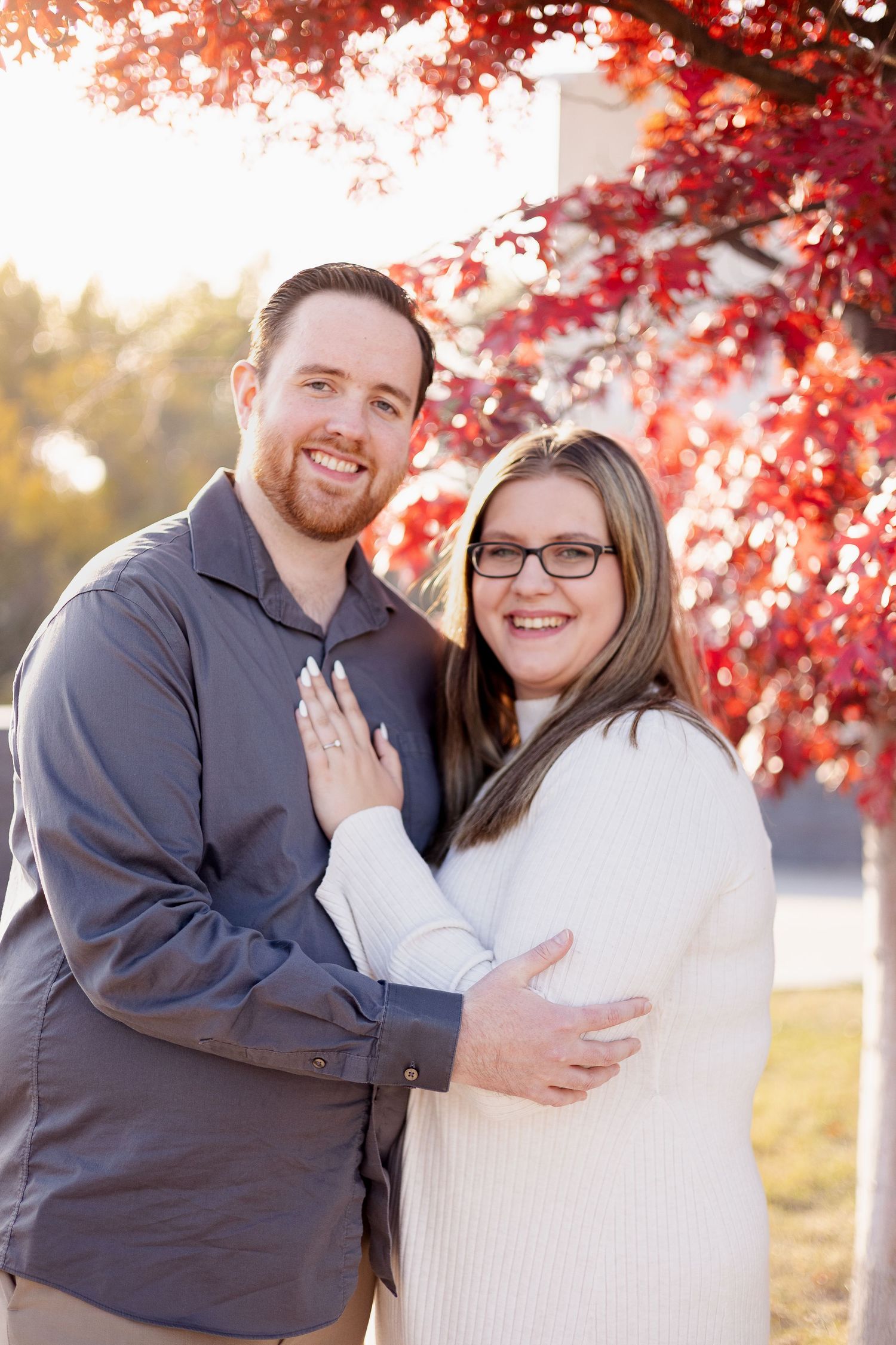 A couple embraces under vibrant red autumn maple leaves during an outdoor photo session.