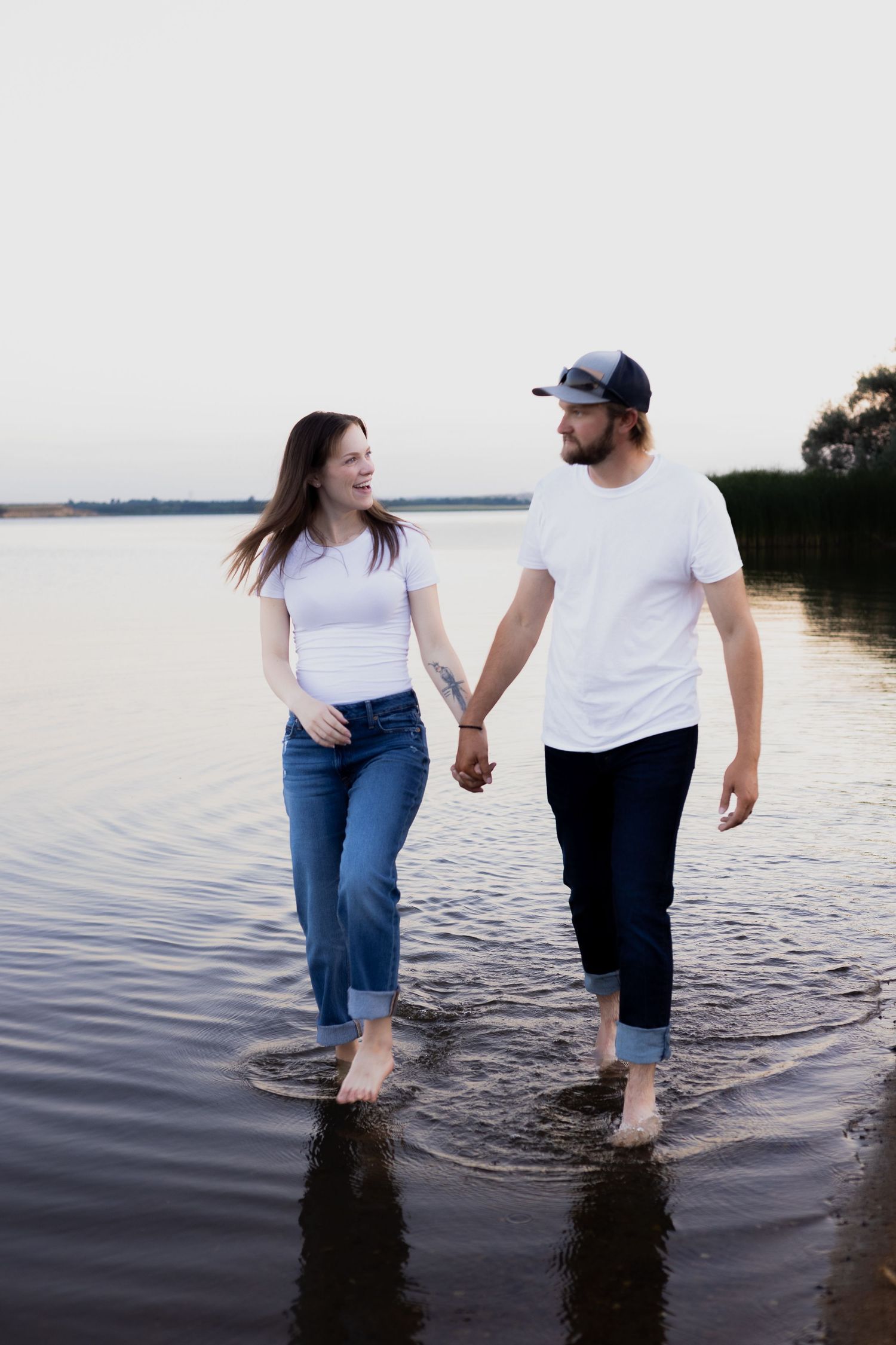 Couple walking hand in hand in shallow water at lakeside.