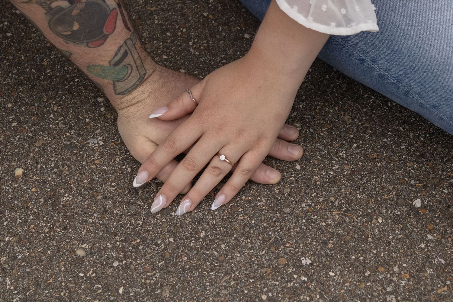 Close-up of hands with engagement ring and tattoo resting on concrete surface.