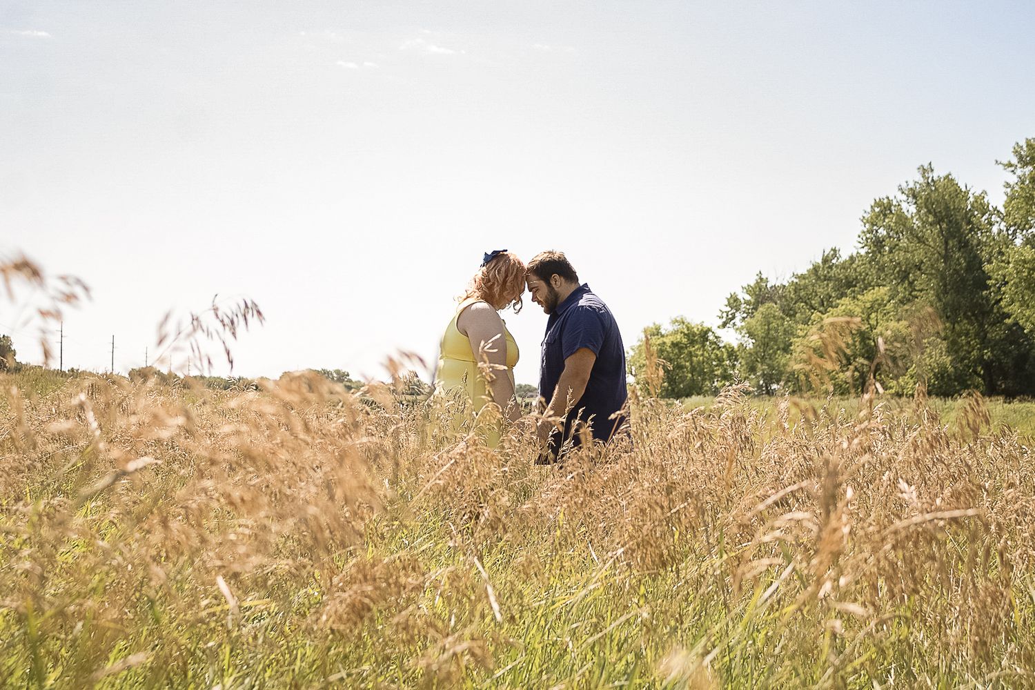 A couple stands together in a sunlit meadow during golden hour.