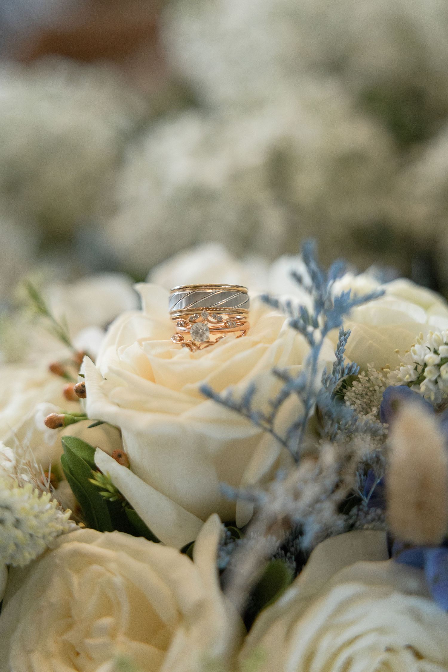 Gold wedding rings nestled among cream roses and blue floral accents.