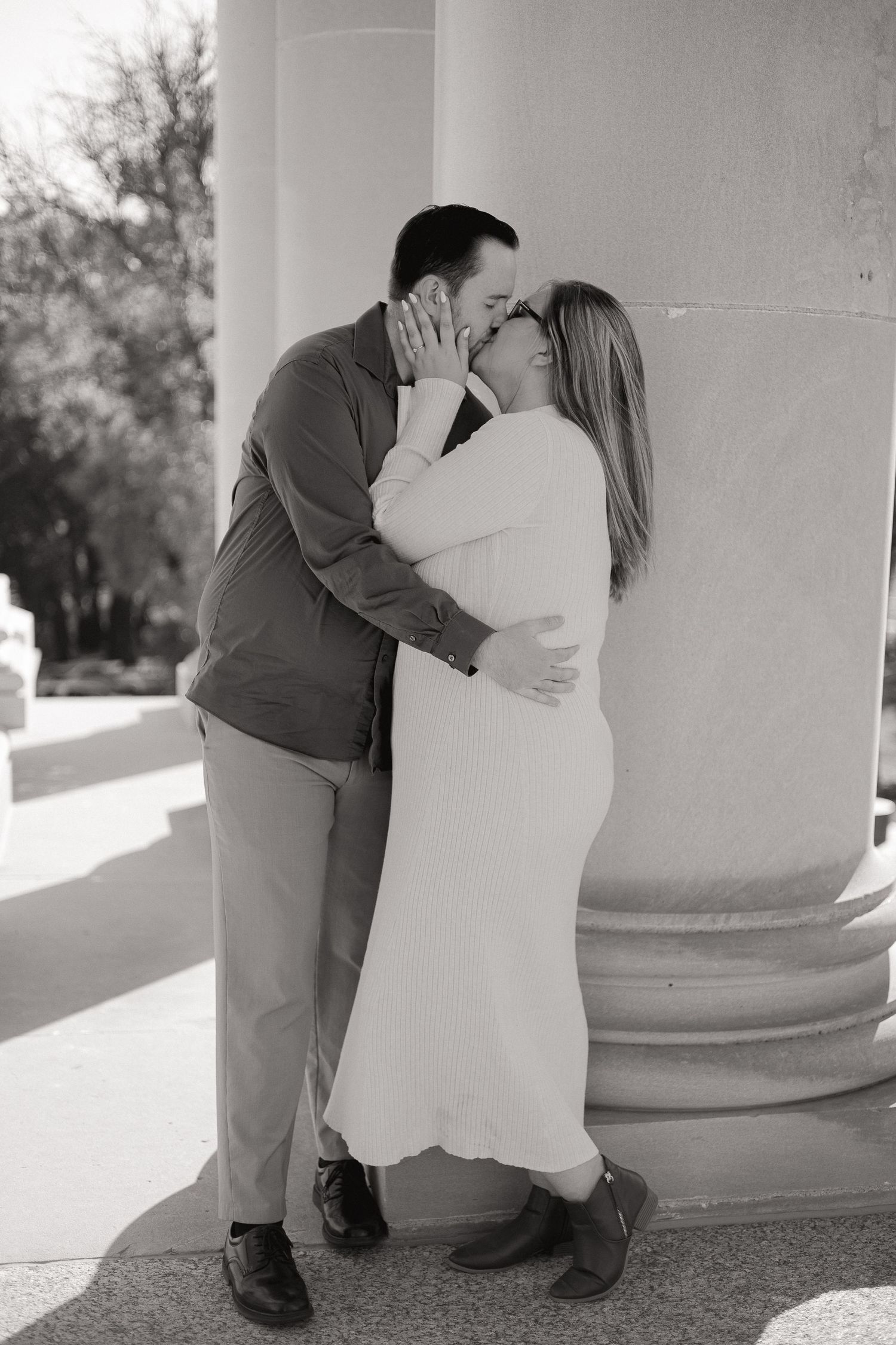 A black and white romantic portrait of a couple embracing by a column.