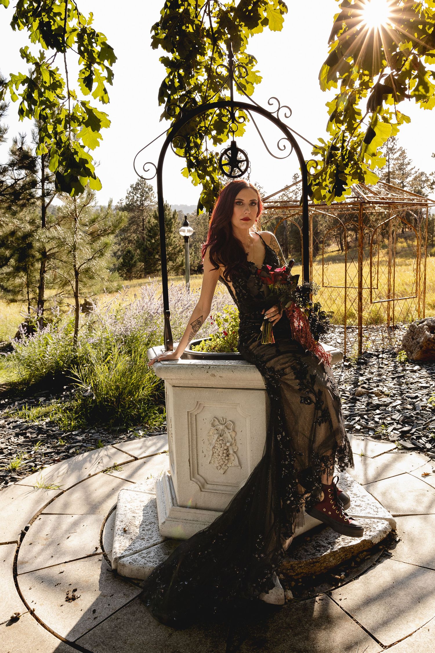 Woman in black dress poses under garden arch during golden hour.