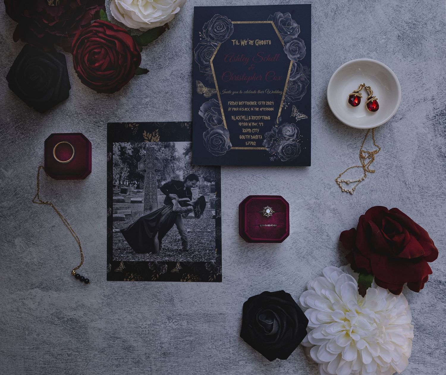 Moody wedding flat lay with dark florals, jewelry boxes, and navy invitation suite.