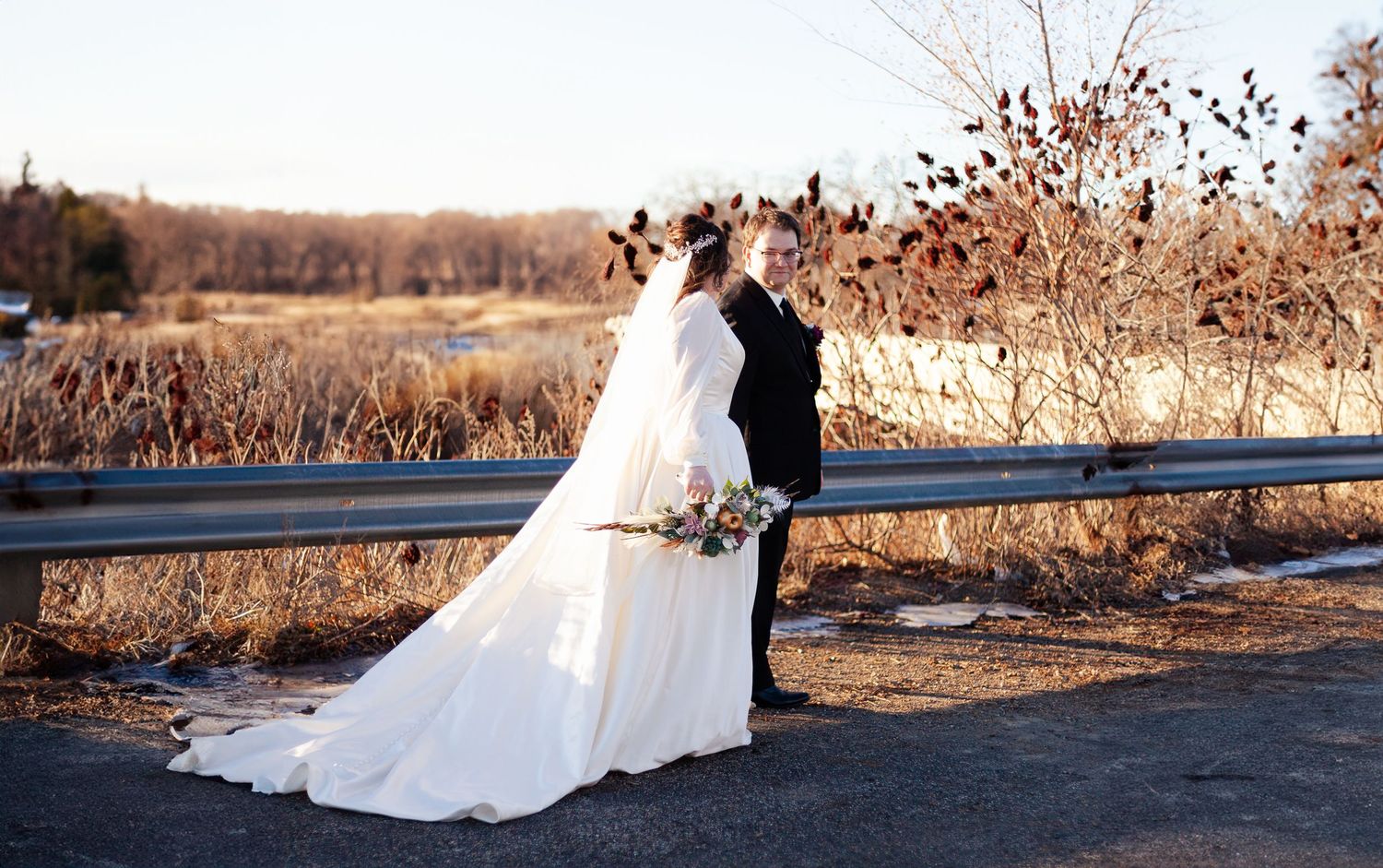 Wedding couple silhouetted against natural autumn landscape with long flowing dress train.