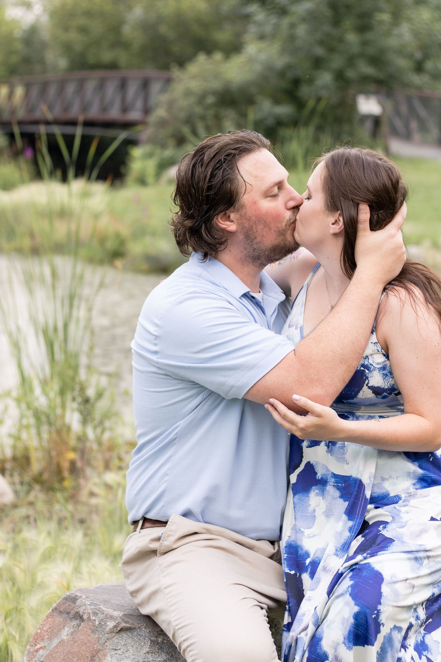 A tender embrace captured by a lake with natural foliage in the background.