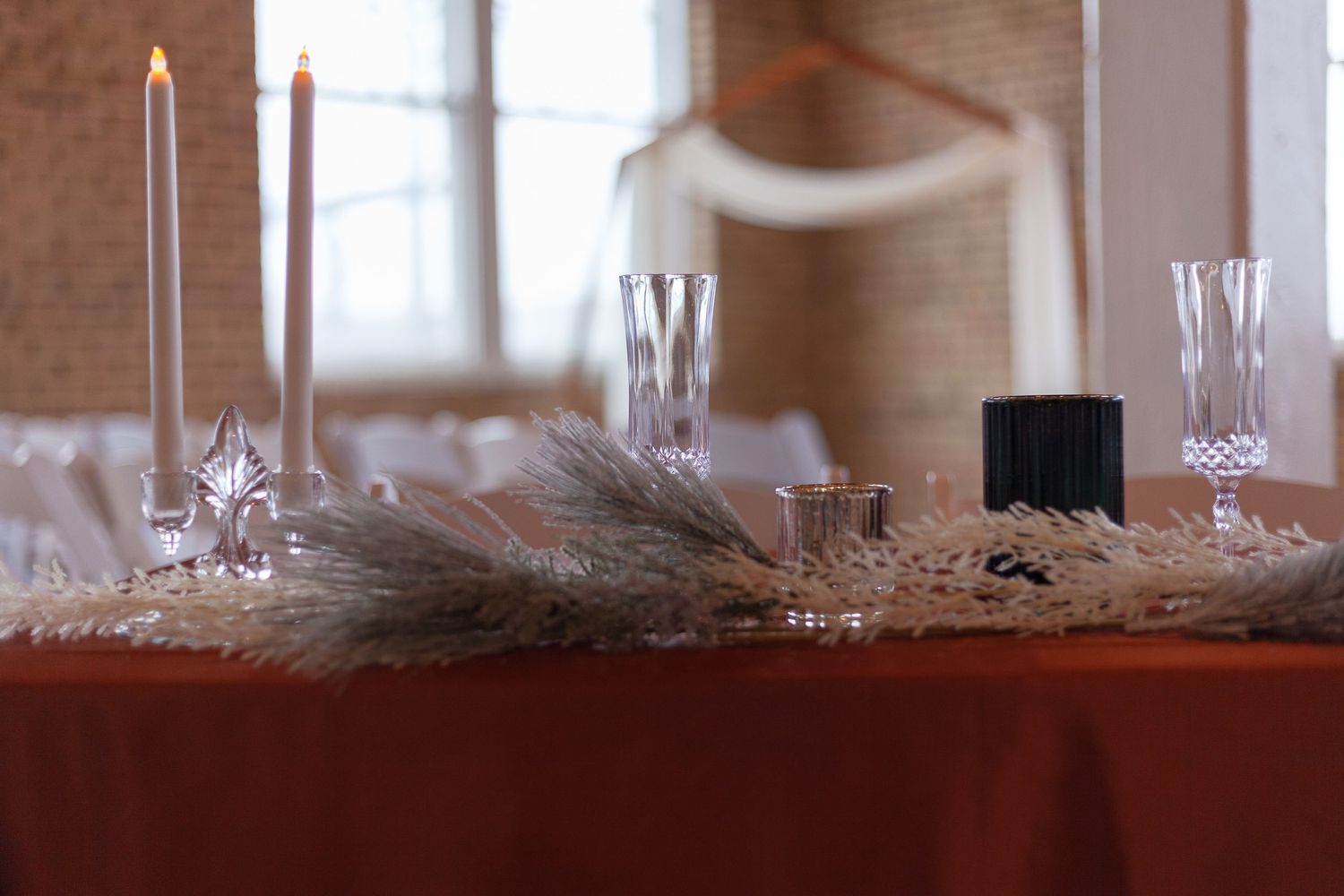 Elegant table setting with candlesticks and feather decor on terracotta tablecloth.