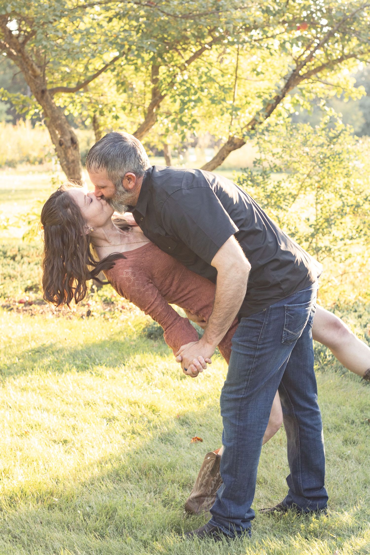 A romantic dip kiss captured in golden sunlight under autumn trees.