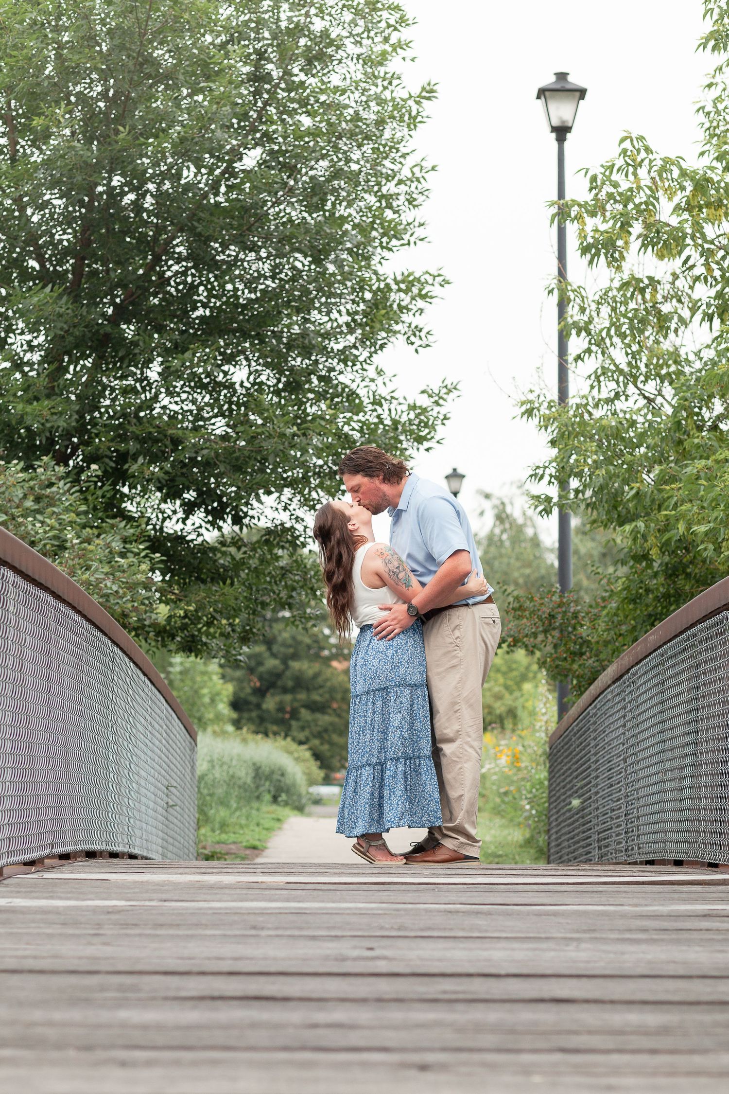 A romantic moment shared on a wooden bridge surrounded by lush greenery and a vintage lamp post.