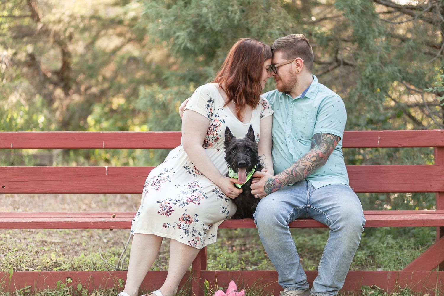 Happy couple shares tender moment on red wooden bench while holding their small dog.