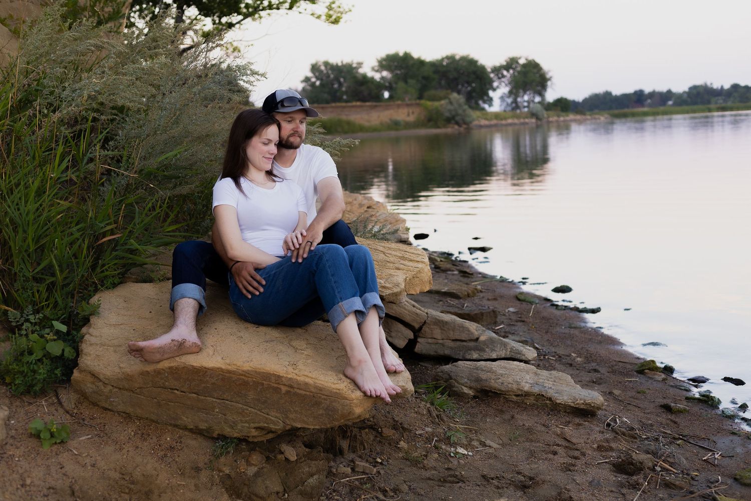 Couple sitting on rocky shoreline during sunset.