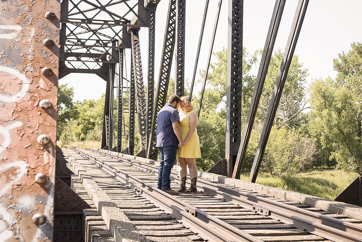 A couple shares an intimate moment on an old railroad bridge surrounded by nature.