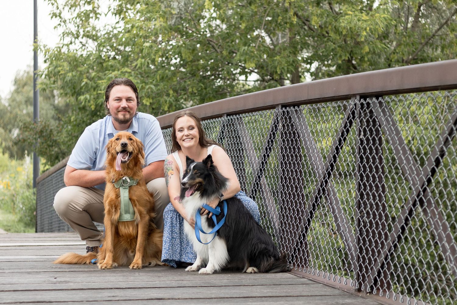 Couple sitting on wooden bridge with their two dogs during outdoor portrait session.