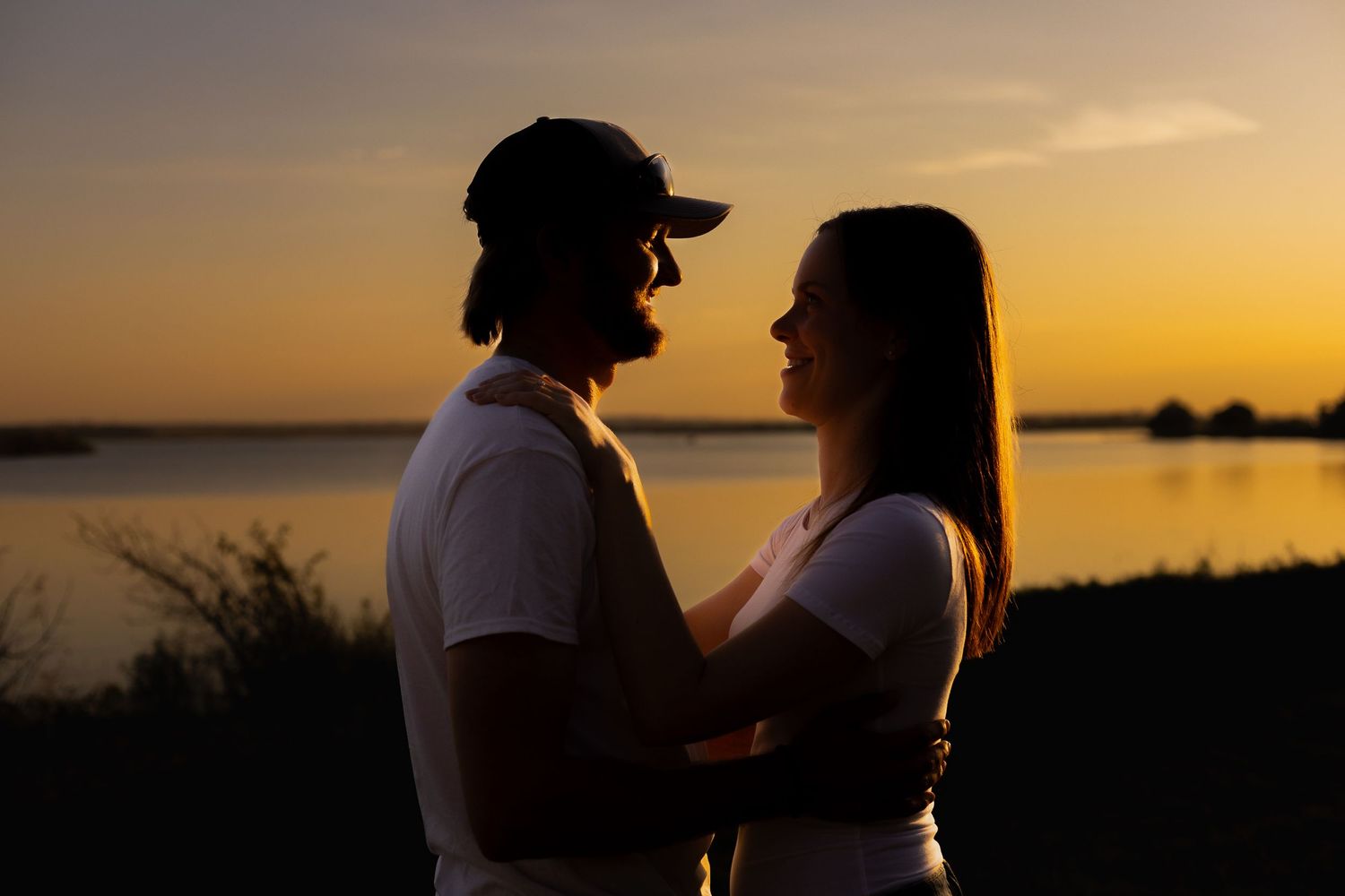 Couple embracing in silhouette against golden sunset over water.