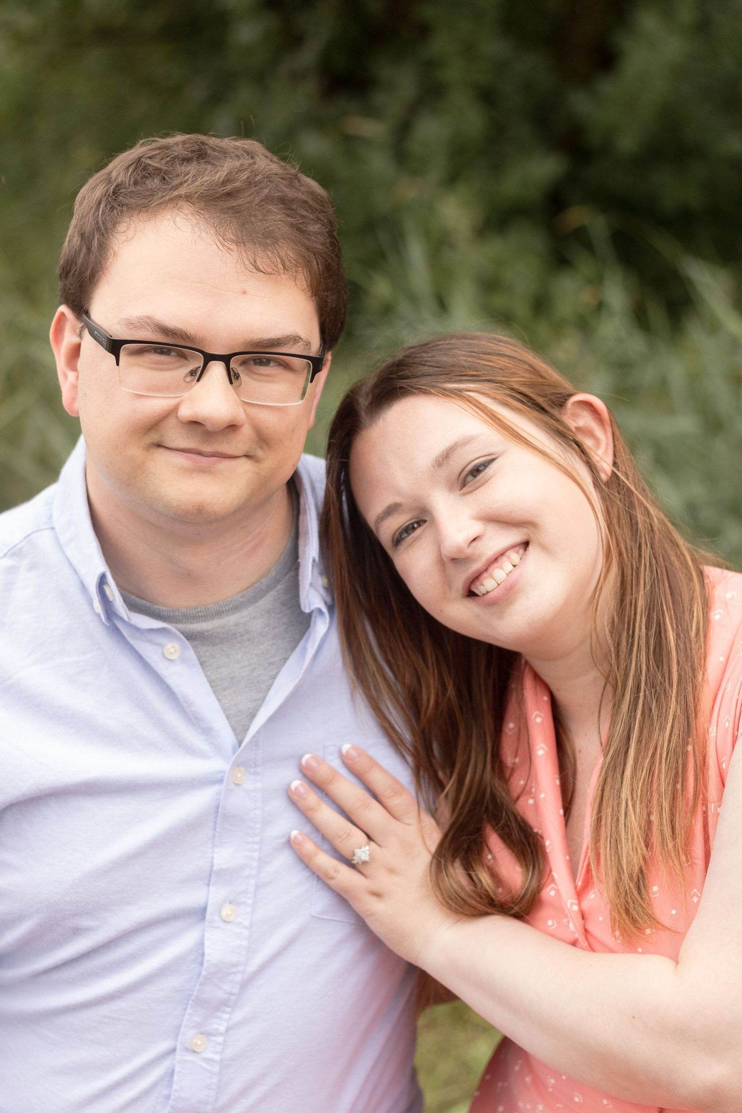 A happy couple poses together for a close-up portrait in casual attire against a natural background.