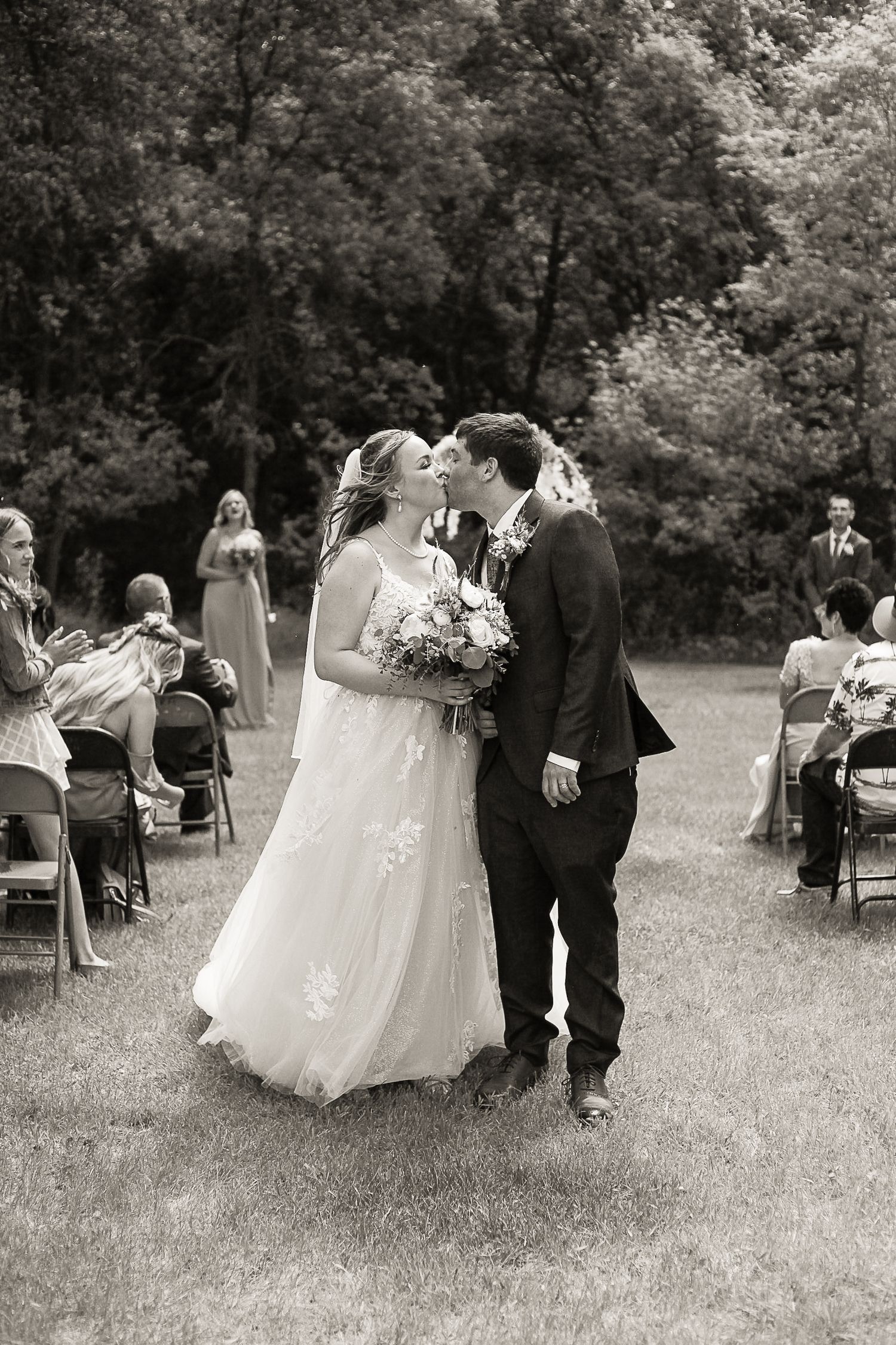 Romantic outdoor wedding ceremony with guests seated on folding chairs.