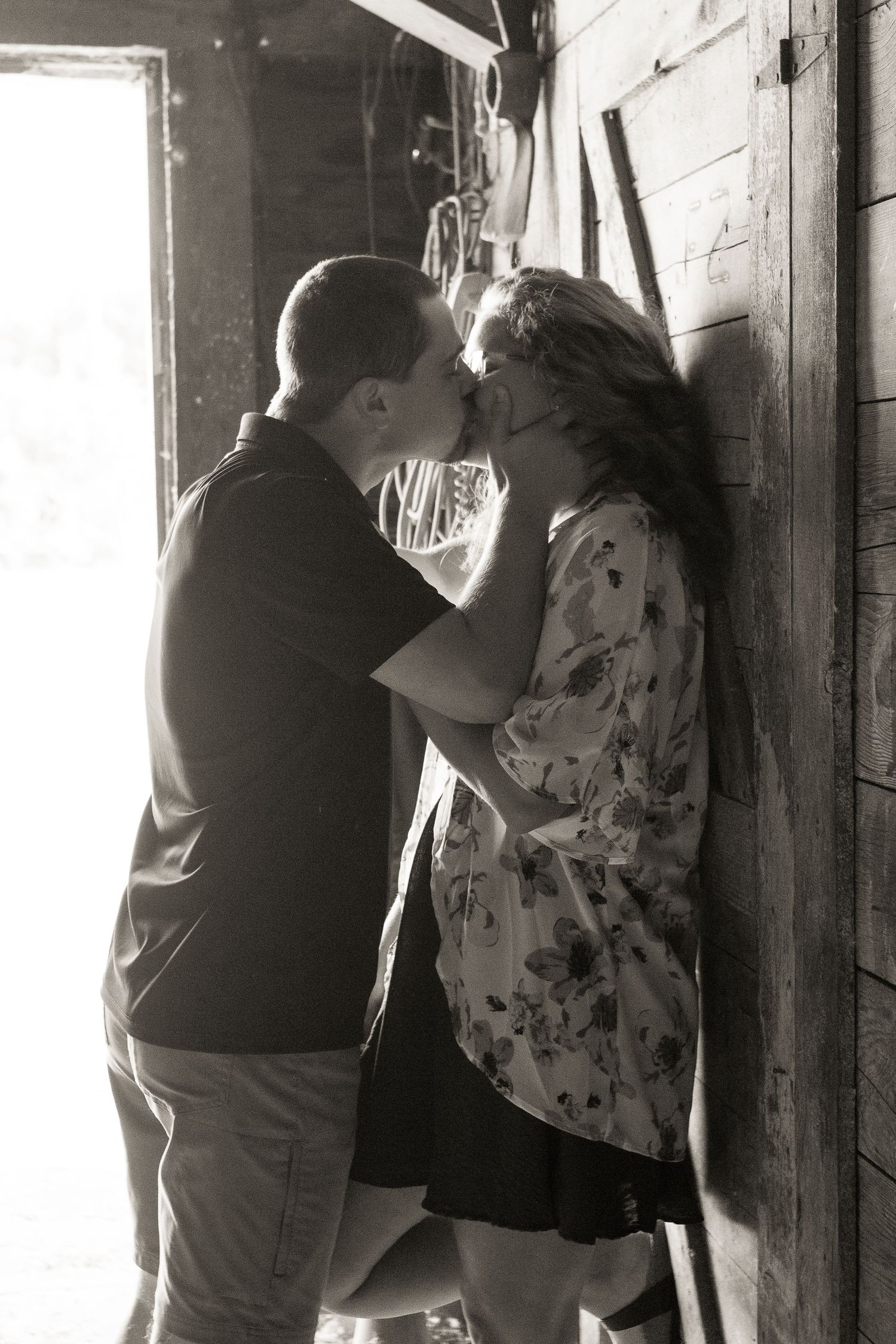 An intimate black and white photo of a couple in a rustic barn setting.